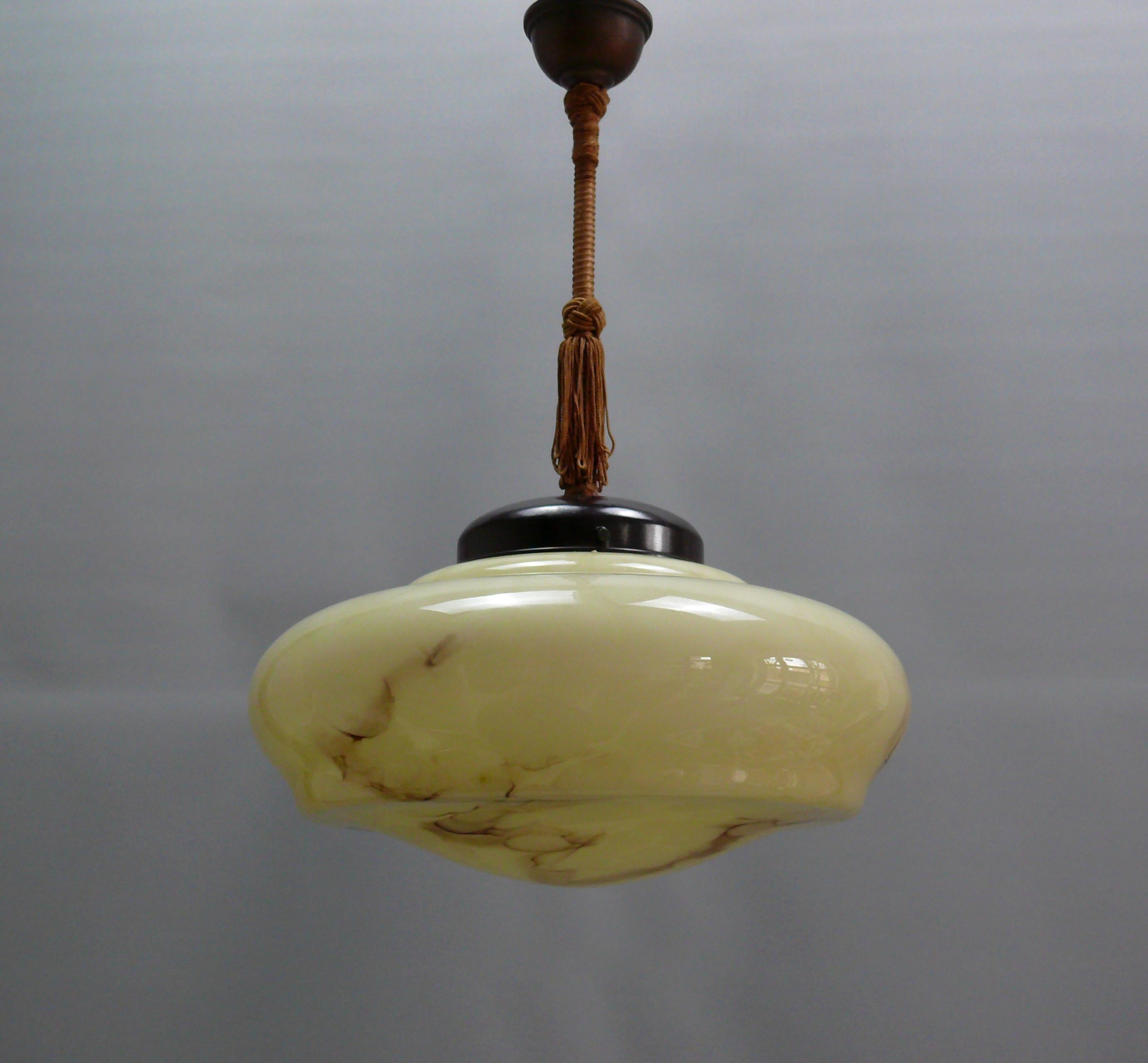 Art Deco rod pendant light from the 1930s-1940s with an elegantly shaped, beige glass shade. The glass shade is marbled and in very good condition. The suspension is made of metal, brass, and Bakelite. The glass holder was replaced from existing
