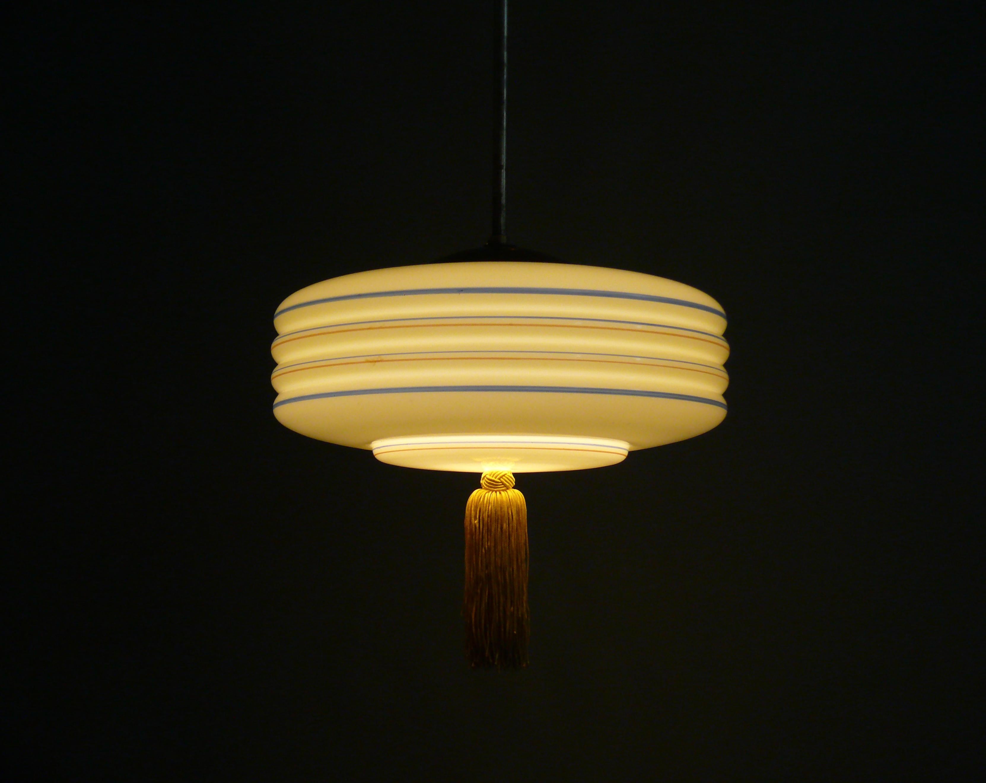 Art Deco rod pendant light with a beige glass shade from the 1930s-1950s. The suspension is made of brass, the glass holder is made of sheet metal. At the bottom of the shade is a period-typical tassel, which has been restored in a matching color