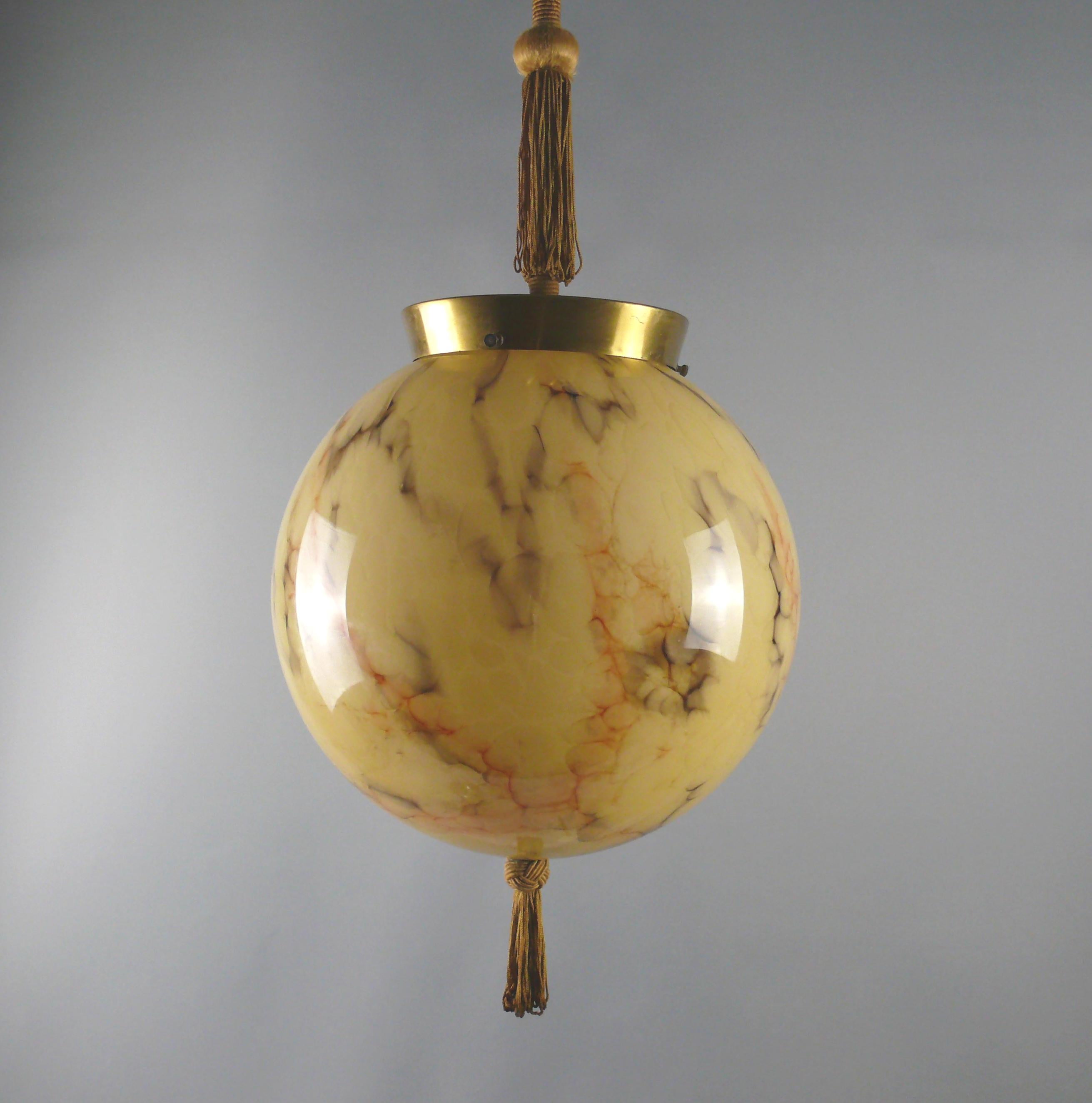 Elegant Art Deco ball lamp with brass suspension, wrapped pendulum rod, tassel and large, marbled glass shade. The beige glass shade is streaked with brown and red stripes. The lamp dates from the first half of the 20th century (1930 - 1950) and is