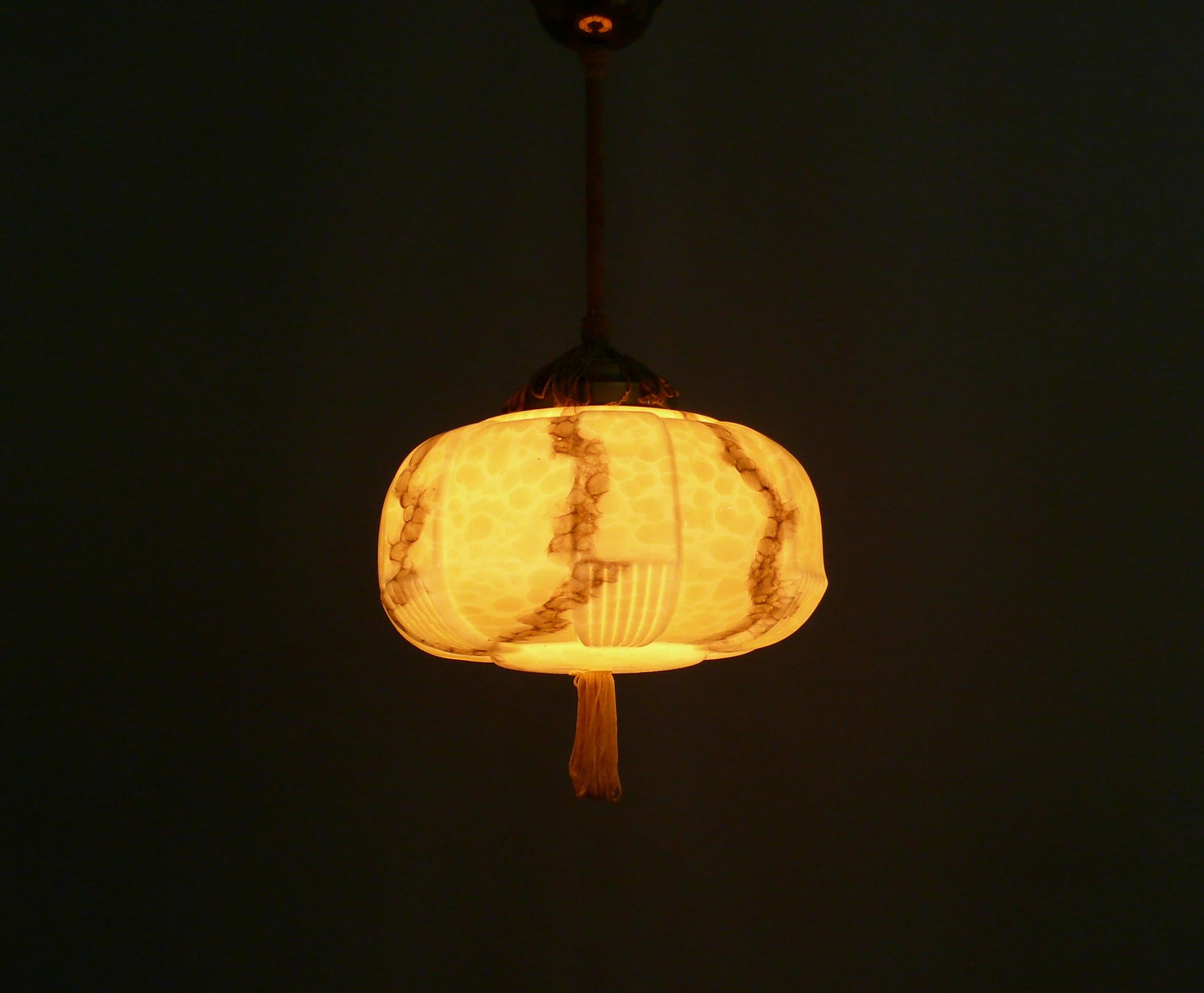 Art Deco rod pendant lamp from the 1930s - 1940s with a very beautiful profiled, beige glass shade in good condition. The glass shade has subtle marbling, profiling and a period-typical tassel on the underside of the shade. The glass holder and the