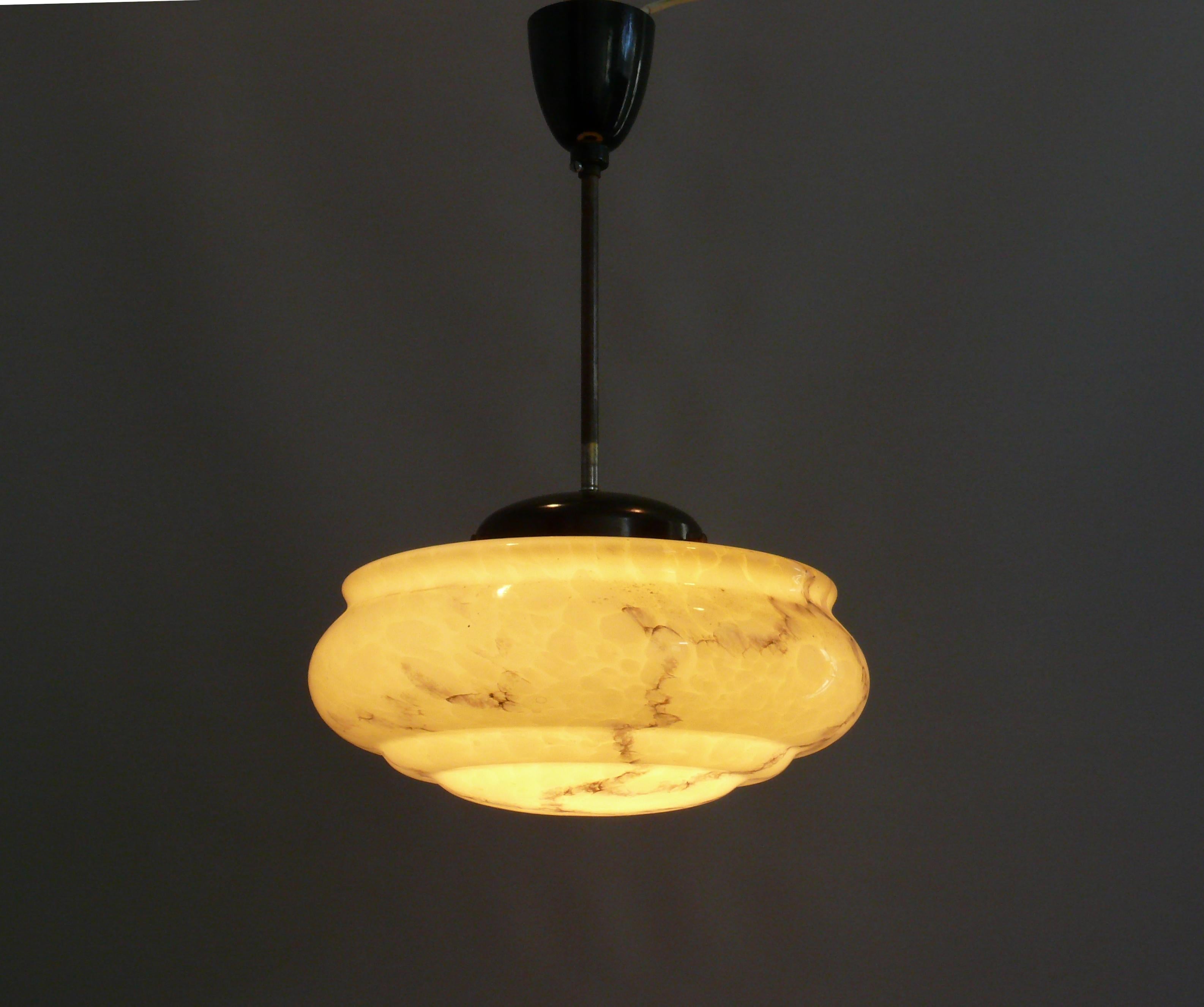 Art Deco rod pendant lamp from the 1930s - 1950s with a very beautiful profiled, beige glass shade in good condition. The glass shade has subtle marbling and profiling on the underside of the shade. The glass holder and the canopy are made of