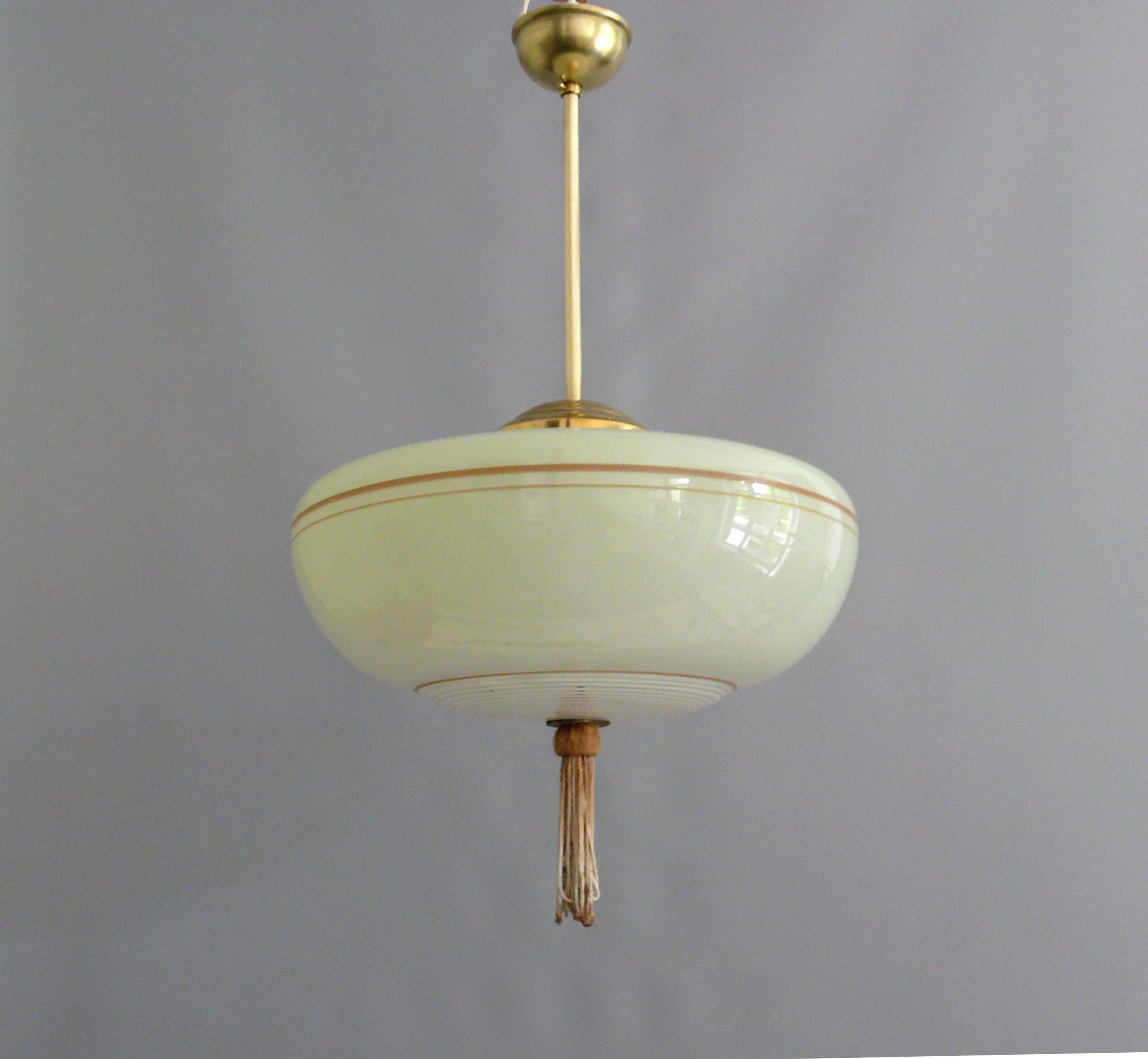 Rod pendant lamp from the 1930s - 1950s with a beige glass shade and brass suspension.

The glass shade has radial decorative stripes in the lower area and a tassel typical of the time in the middle at the bottom. The glass holder, rod and canopy
