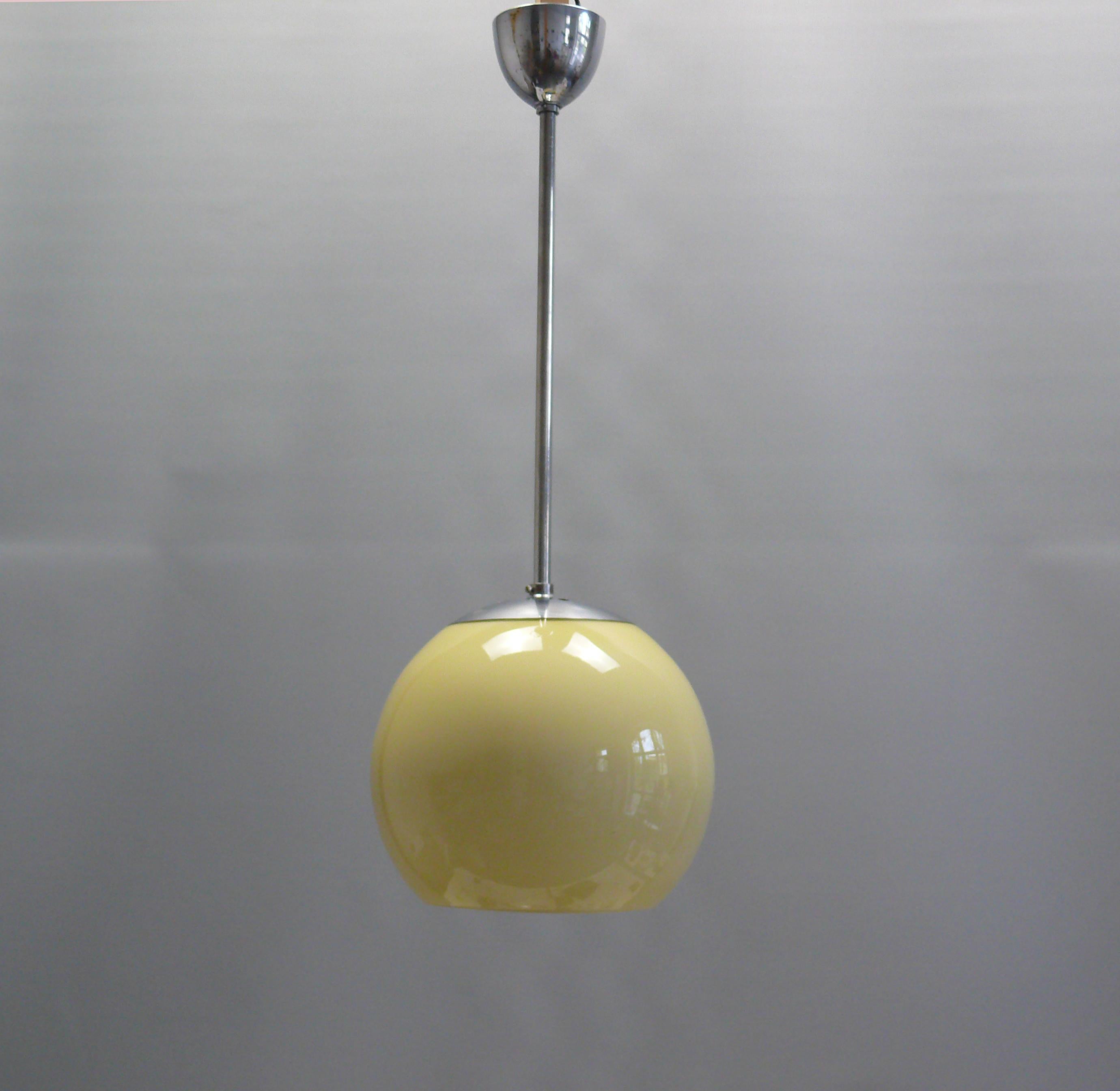 Elegant Bauhaus pendant lamp with a spherical shade made of yellowish opal glass with a chrome-plated metal suspension and pendulum rod. The lamp dates from the first half of the 20th century (1920 - 1940) and is in good, functional original