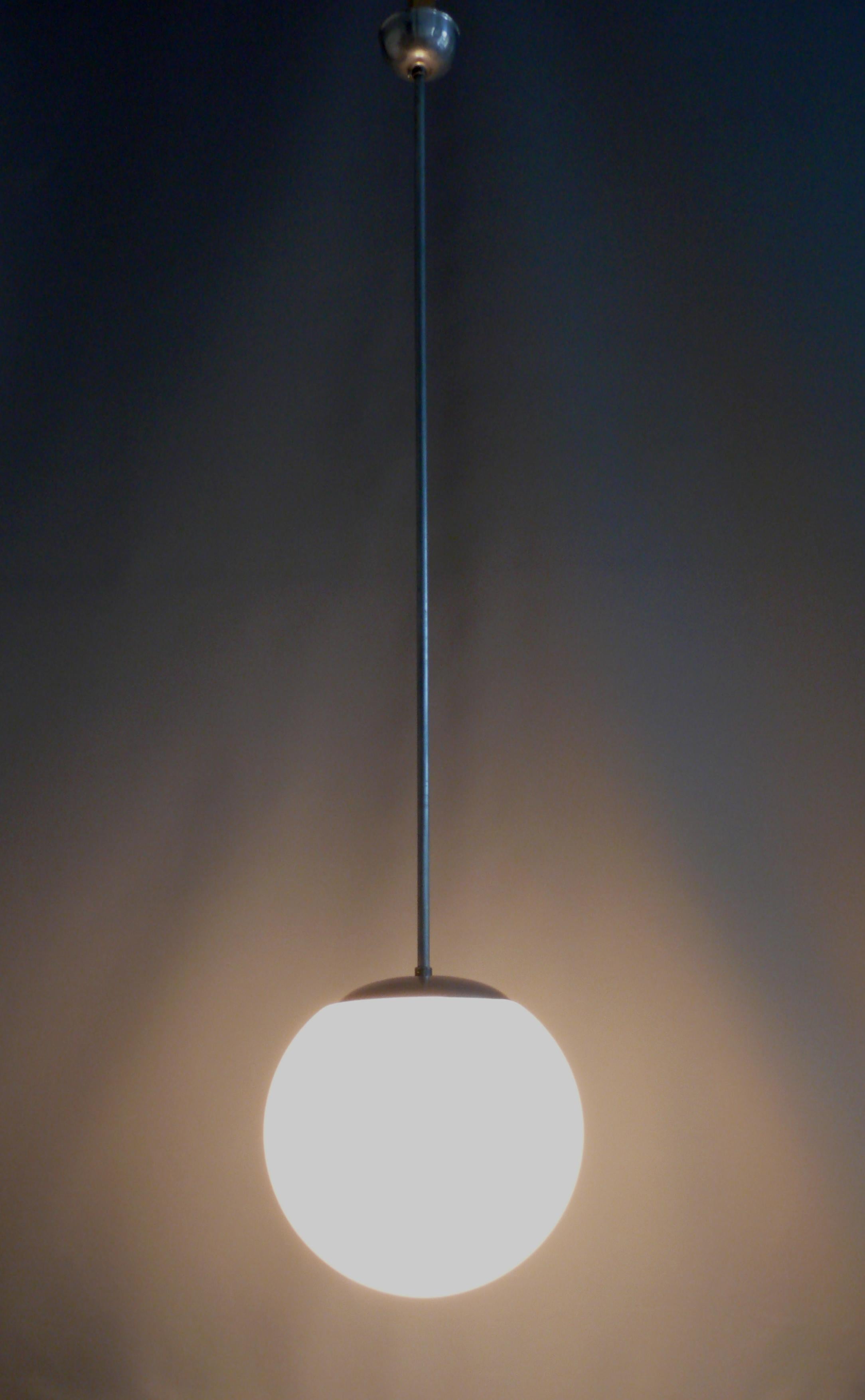 Elegant Bauhaus spherical lamp made of opal glass with a metal suspension and a very long pendulum rod. The lamp dates from the first half of the 20th century (1920-1940) and is in good, working condition*. The surfaces of the metal parts (probably