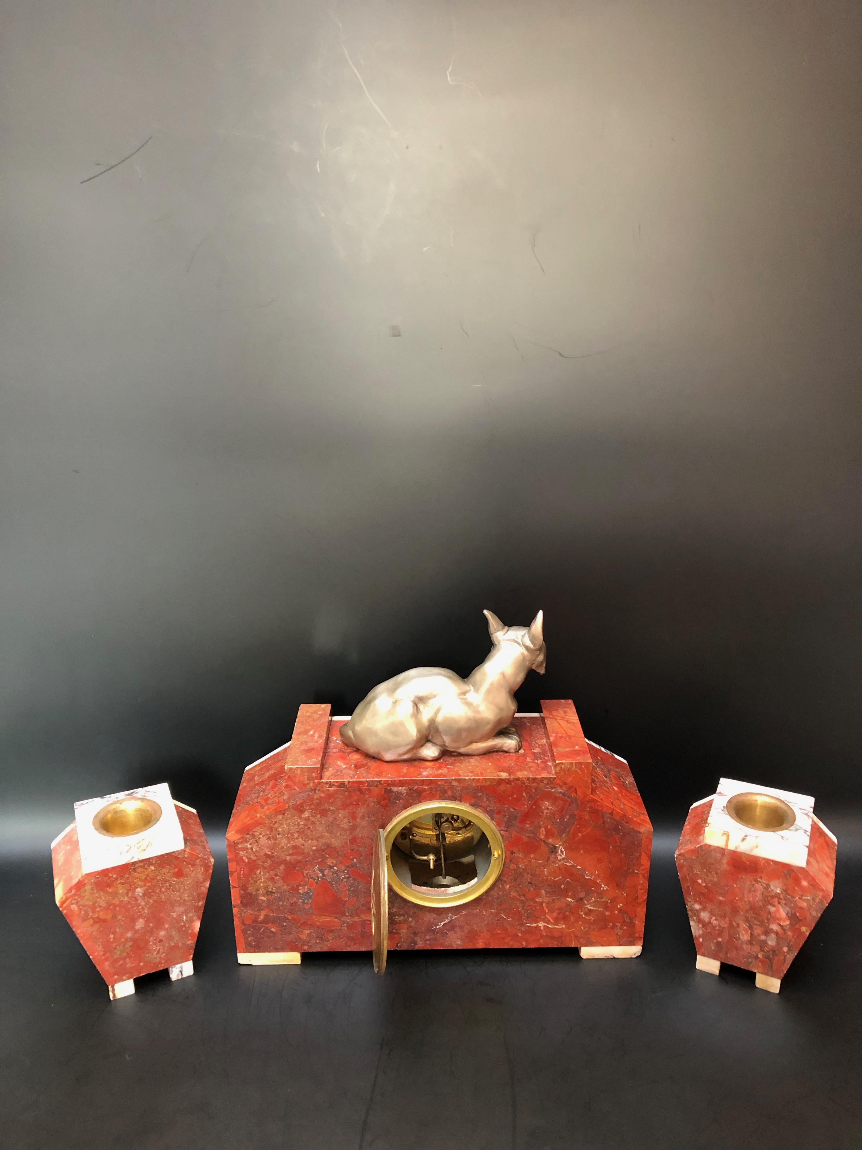 Pendule vers 1930 en marqueterie de marbre rouge et blanc veiné. Surmonté d'un chat en bronze argenté accompagné de ses 2 cassollets
Mécanisme estampillé 