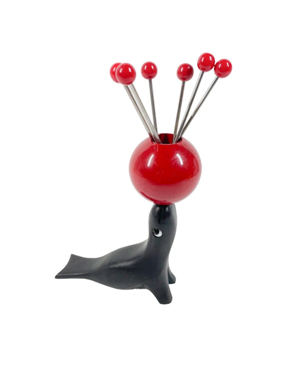 Art Deco cocktail pick set, carved and painted wood seal with glass eyes balancing a red painted wood ball on its nose with six Bakelite topped metal cocktail picks. 