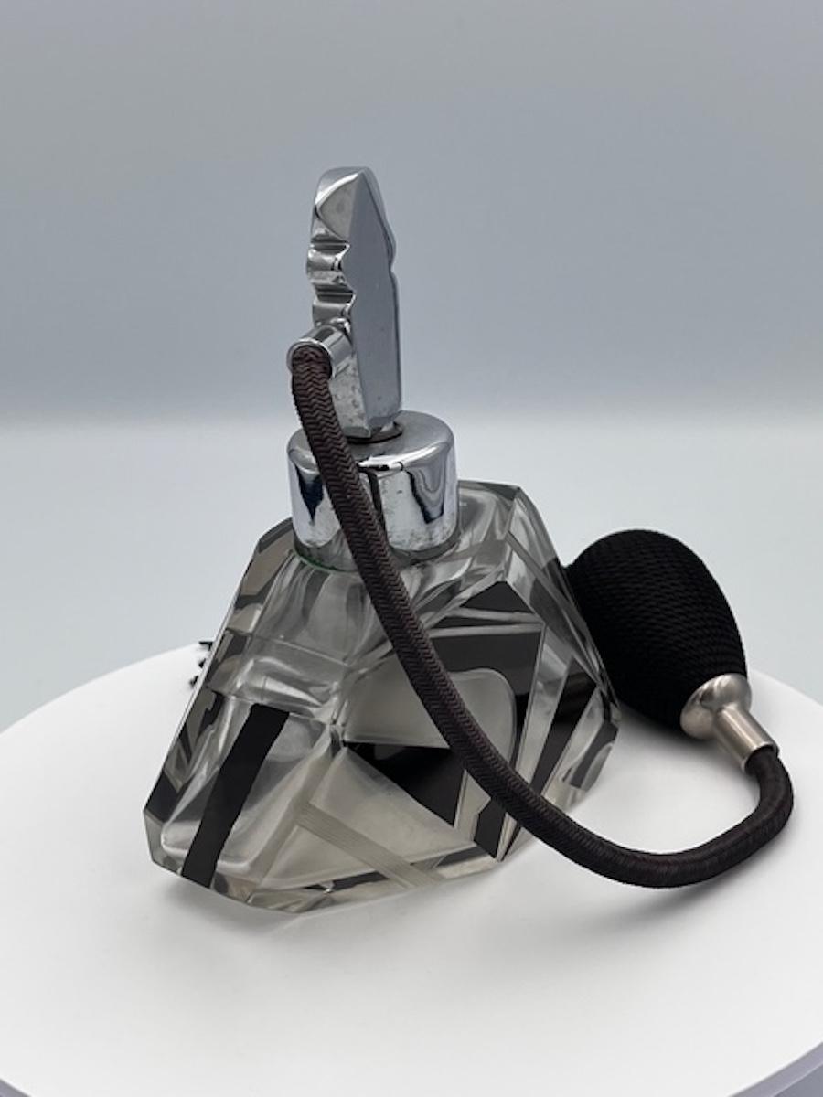 Questo squisito flacone di profumo Art Déco è un esempio straordinario della maestria di Karl Palda nel design geometrico e nell'artigianato. Realizzata in vetro tagliato e inciso, la bottiglia presenta un elegante motivo a smalto nero che enfatizza