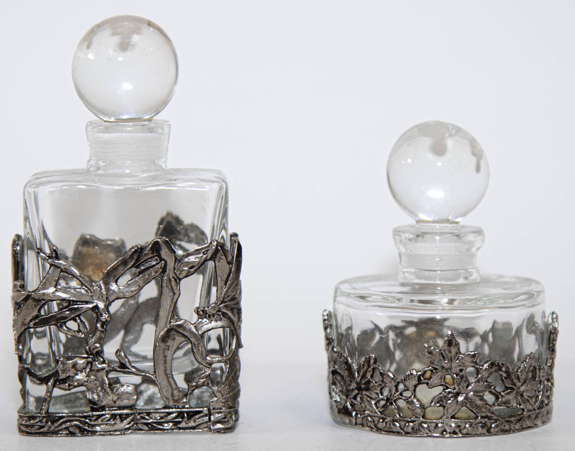 Art Deco style perfume bottles featuring clear glass with intricate silver metal overlay.
Vintage empty glass and pewter silver cast metal decorative small perfume bottles.
Set of two nice functional or decorative pieces for your dressing