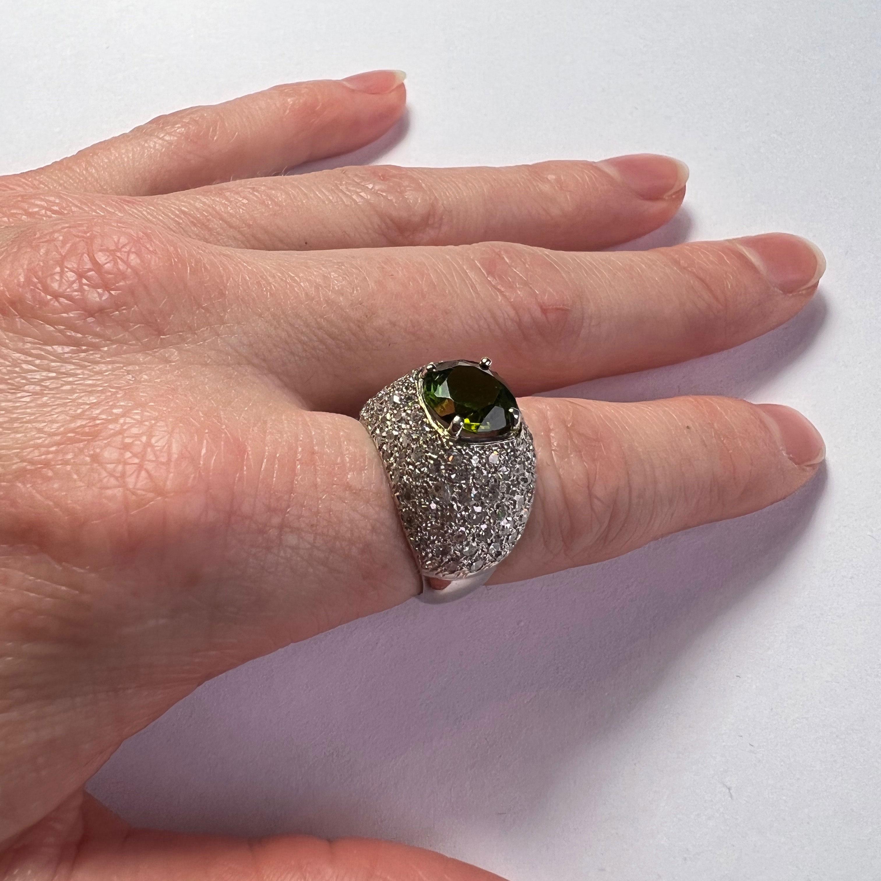 A beautifully made platinum ring set with a cushion cut peridot in a field of pave set round single cut diamonds.
Unmarked, but the quality and style of manufacture is reminiscent of rings made by Henri Picq for Cartier.

Ring size: J.5 (US size