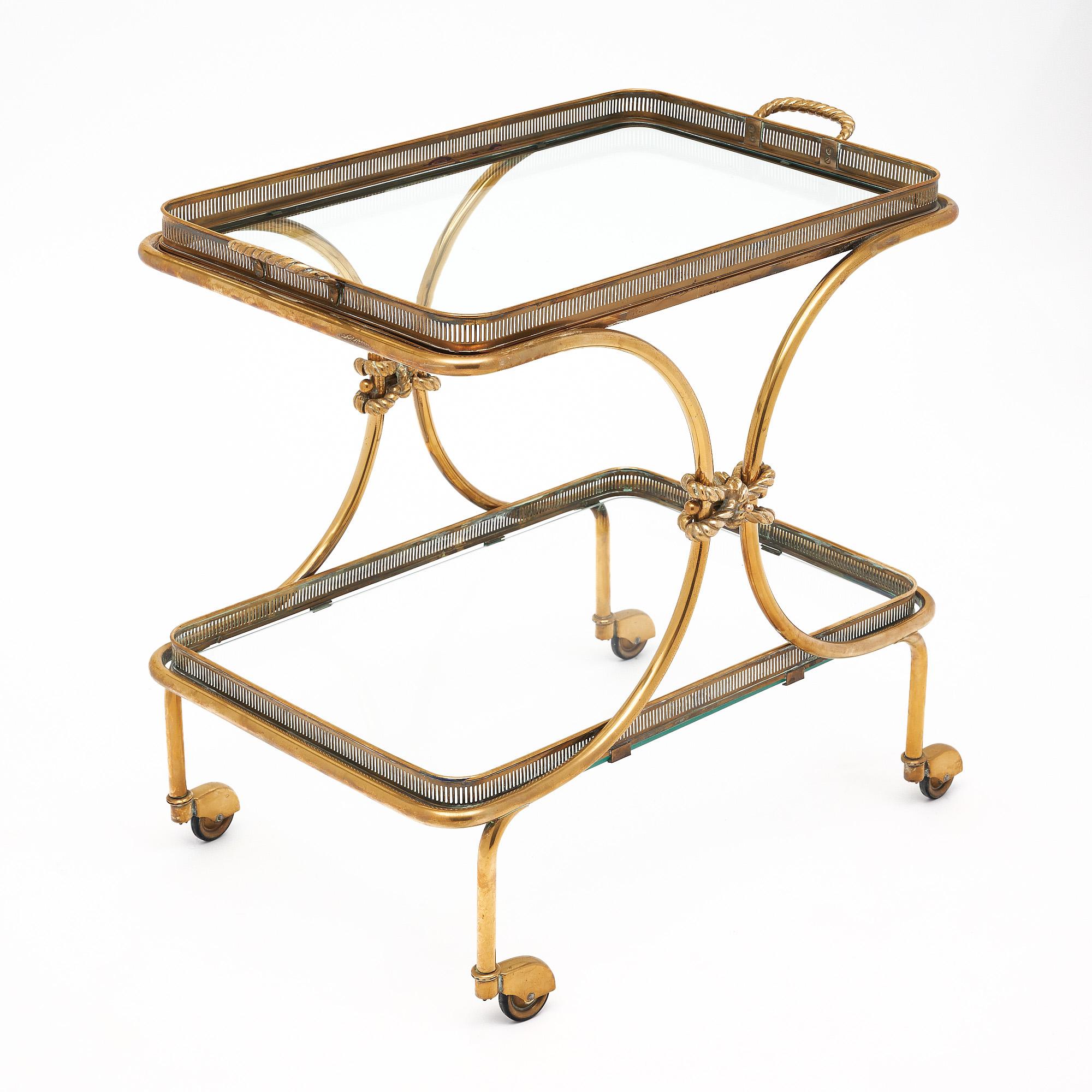 Brass bar cart from the Art Deco period in France. This piece is rectangular in shape with two shelves of glass. The top shelf lifts off as a tray for functionality. Both shelves feature open brass galleries. The structure has curved sides adorned