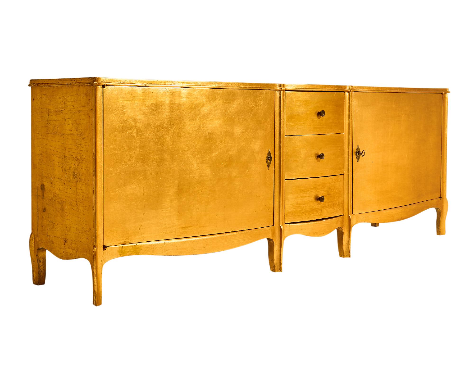 Buffet / enfilade from the Art Deco period in France made of beech wood that has been finished with a gold leaf lacquer. There are two doors that open to interior shelving and four dovetailed drawers down the center. We love the Art Deco curves of