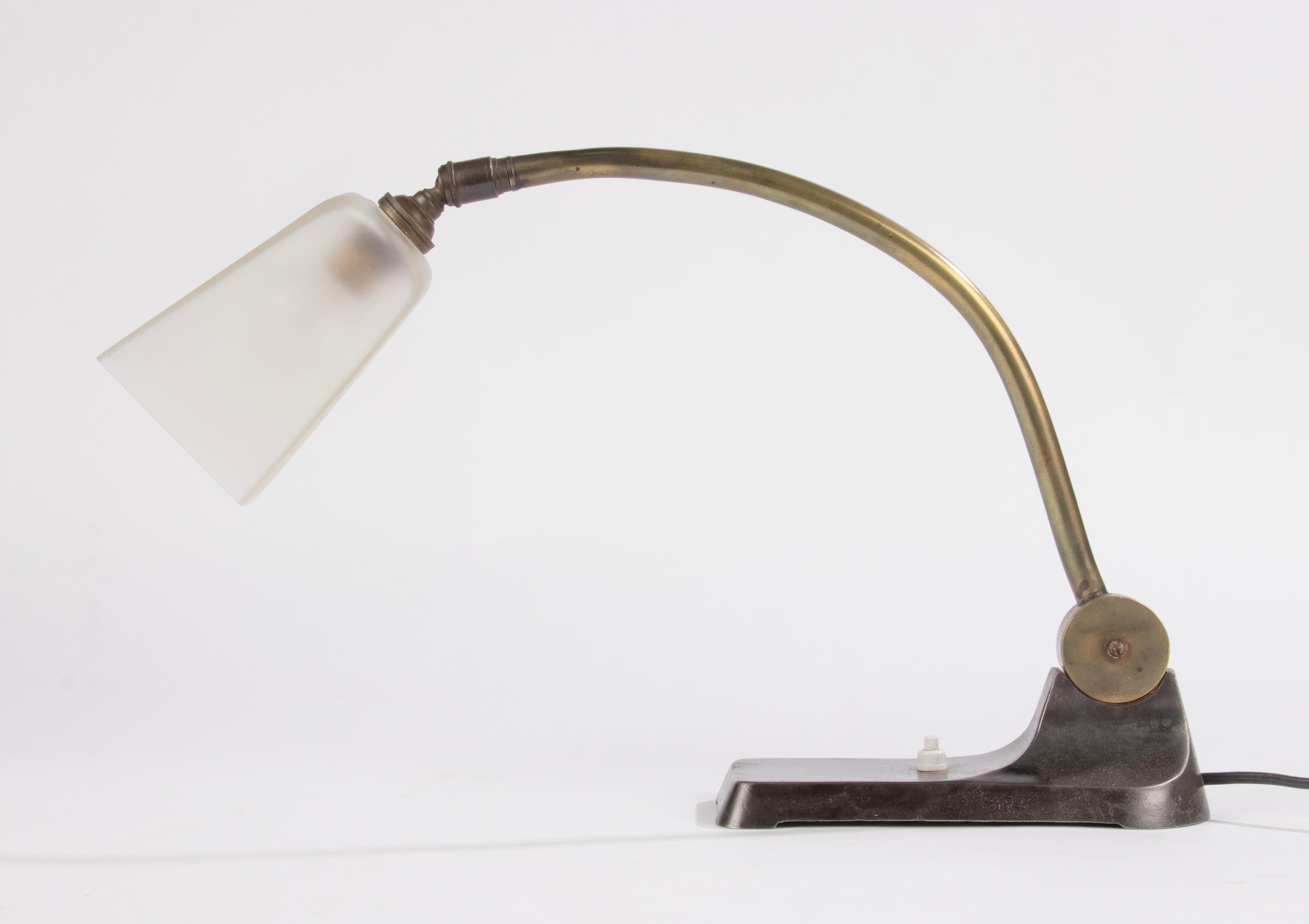 Beautiful Art Deco desk lamp in industrial style. The base is made of cast iron, the arm is made of bronze and is adjustable. The shade is made of sanitized glass. 
The lamp functions and in is in good condition, with a beautiful original patina.