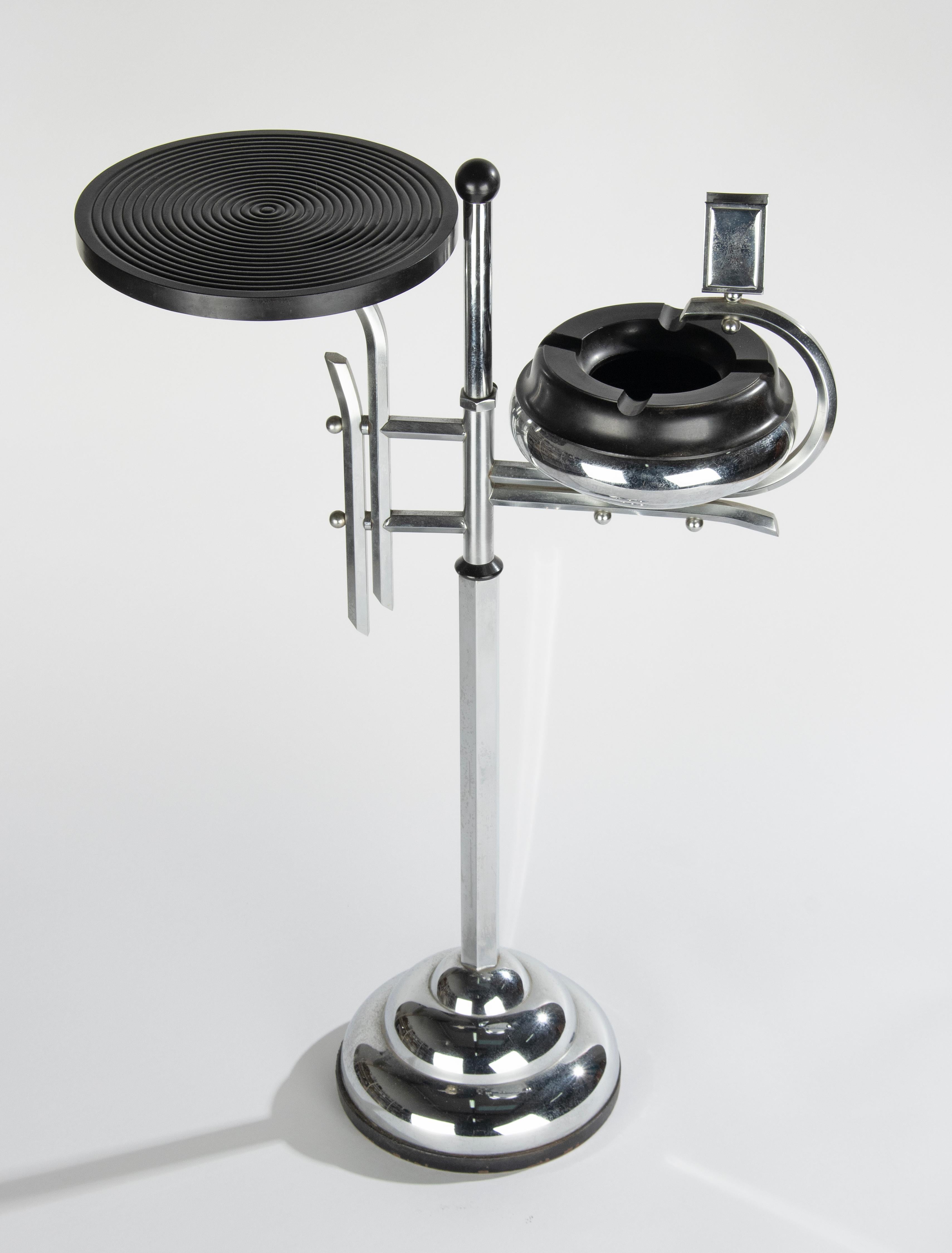 And Art Deco period standing ashtray with tray for drinks and match holder. Made of chrome plated metal and bakelite. It can be turned around. The inside of the foot is off cast iron. Very decorative and Bauhaus design. 
All in good condition, no