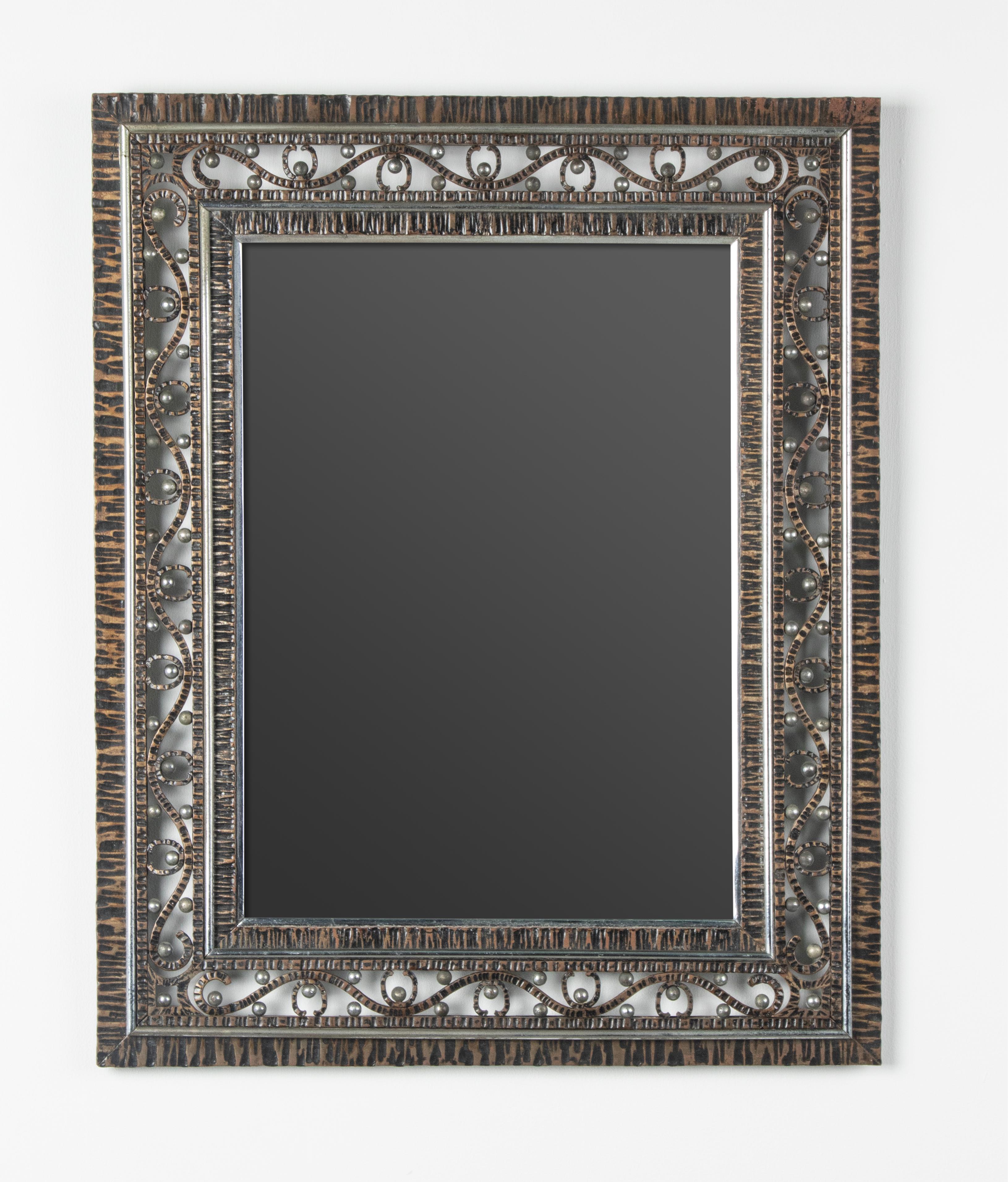 An elegant wall mirror from the French Art Deco period. The frame is made of hand-forged iron, the ironwork is partly patinated, which is original. A border of scrolls with small metal balls, framed wit chrome plated trims. Made in France, circa