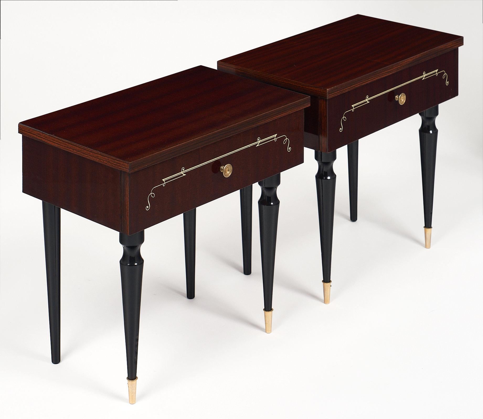 Elegant French Art Deco side tables made of mahogany, each with one drawer and a brass knob. This mod pair has ebonized, tapered legs with brass feet. Each drawer has lovely inlays across the facade as well.