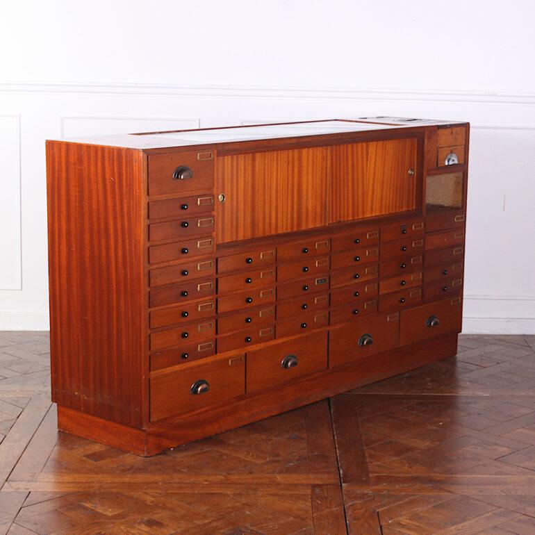 An unusual English Art Deco shop counter / jeweler's or watchmaker's cabinet in mahogany, the clean geometric form typical of the 1930s, fitted with mulitple drawers to the reverse side and with a built in cash drawer. Display section with glass