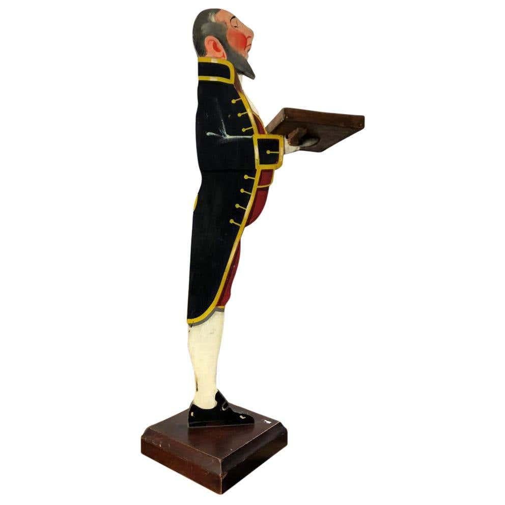 An Art Deco period gentleman waiter, painted wooden figures holding a rectangular tray and standing upon a square plinth. A fine quality pair, often used as card holders for a restaurant or hotel. Ready for home shipping right away. All our shipping