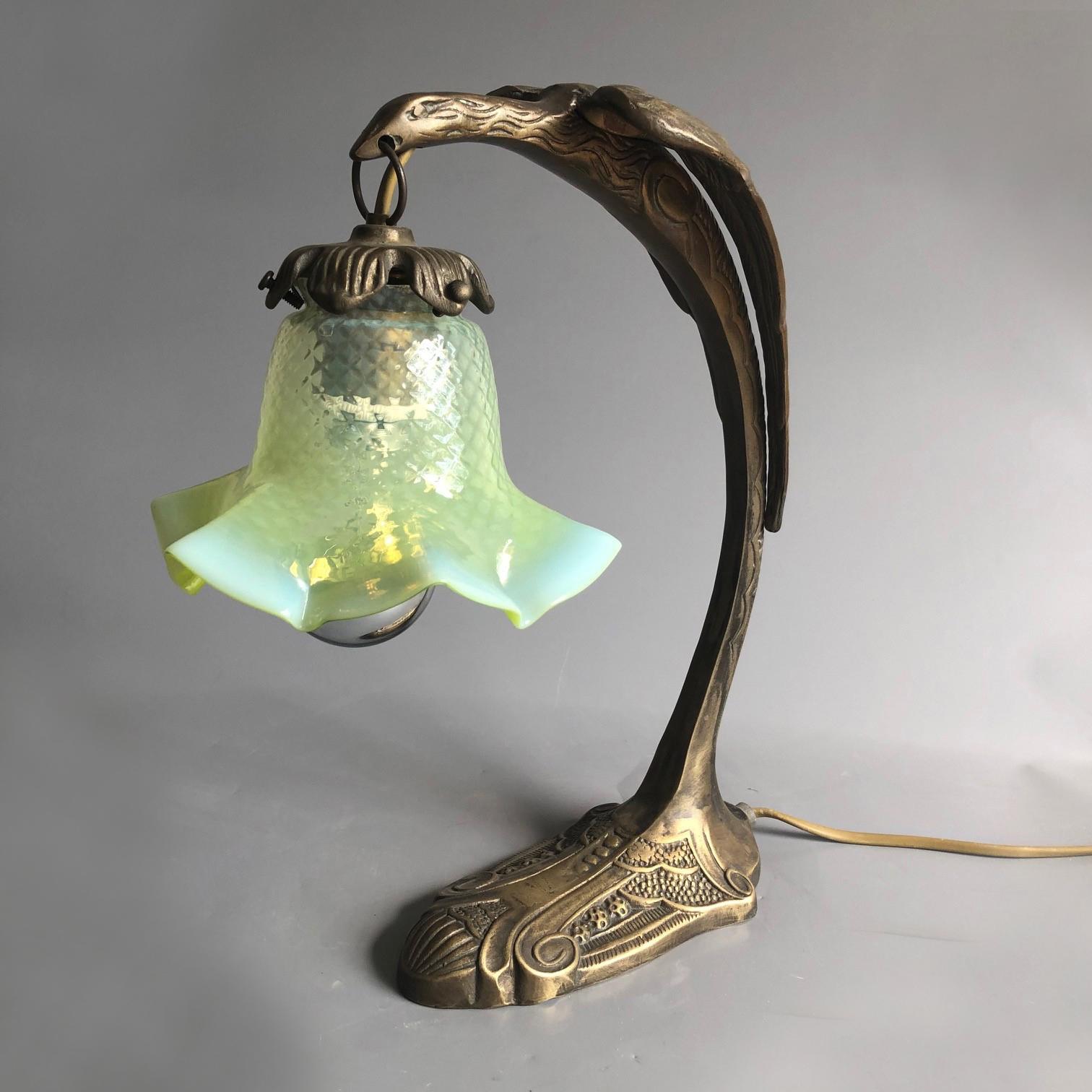 A table lamp in form of a elongated falcon holding a petroleum glass tulip shade in his beak.
E27 light bulb fitting
European 2 pin plug

