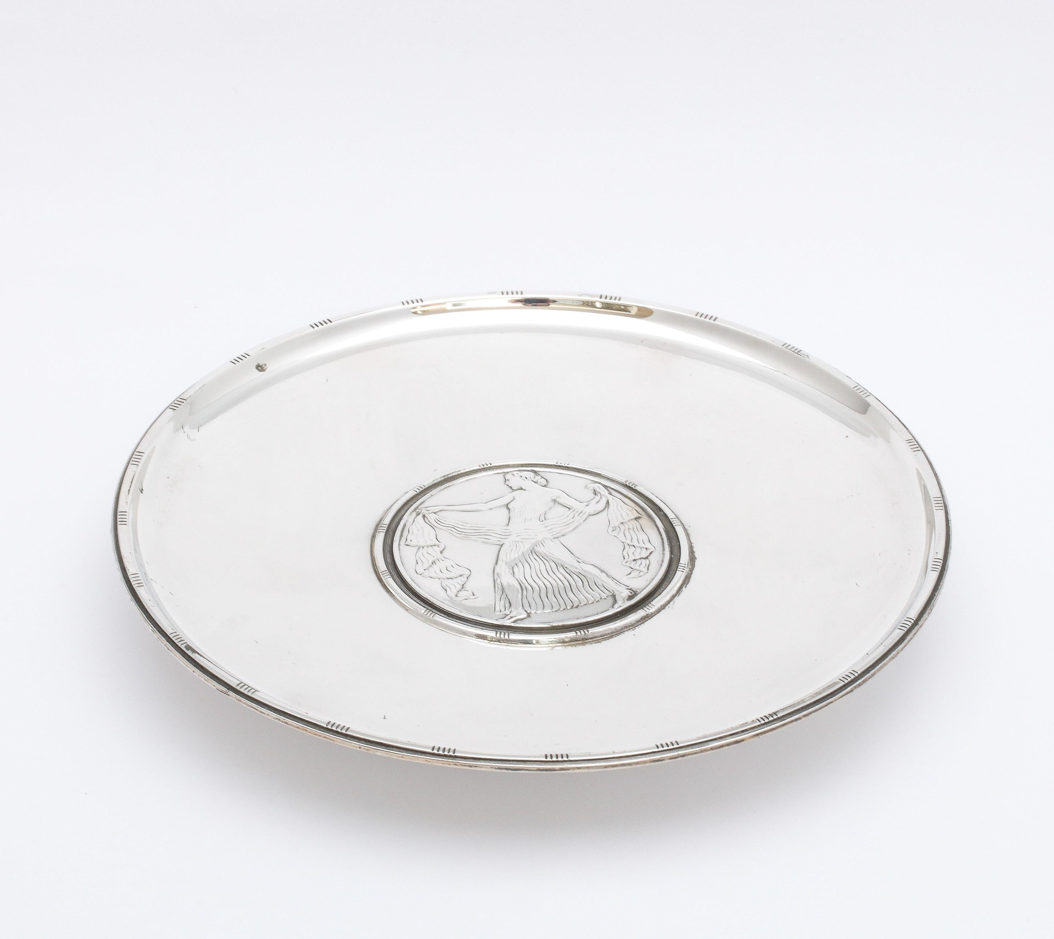 Unusual, Art Deco, sterling silver round serving platter on pedestal base, Tiffany and Co., New York, year-inventory marked for 1924-1925. Designed with an Art Deco figure in the center of the platter. Measures 7 inches diameter x 1 inch high.