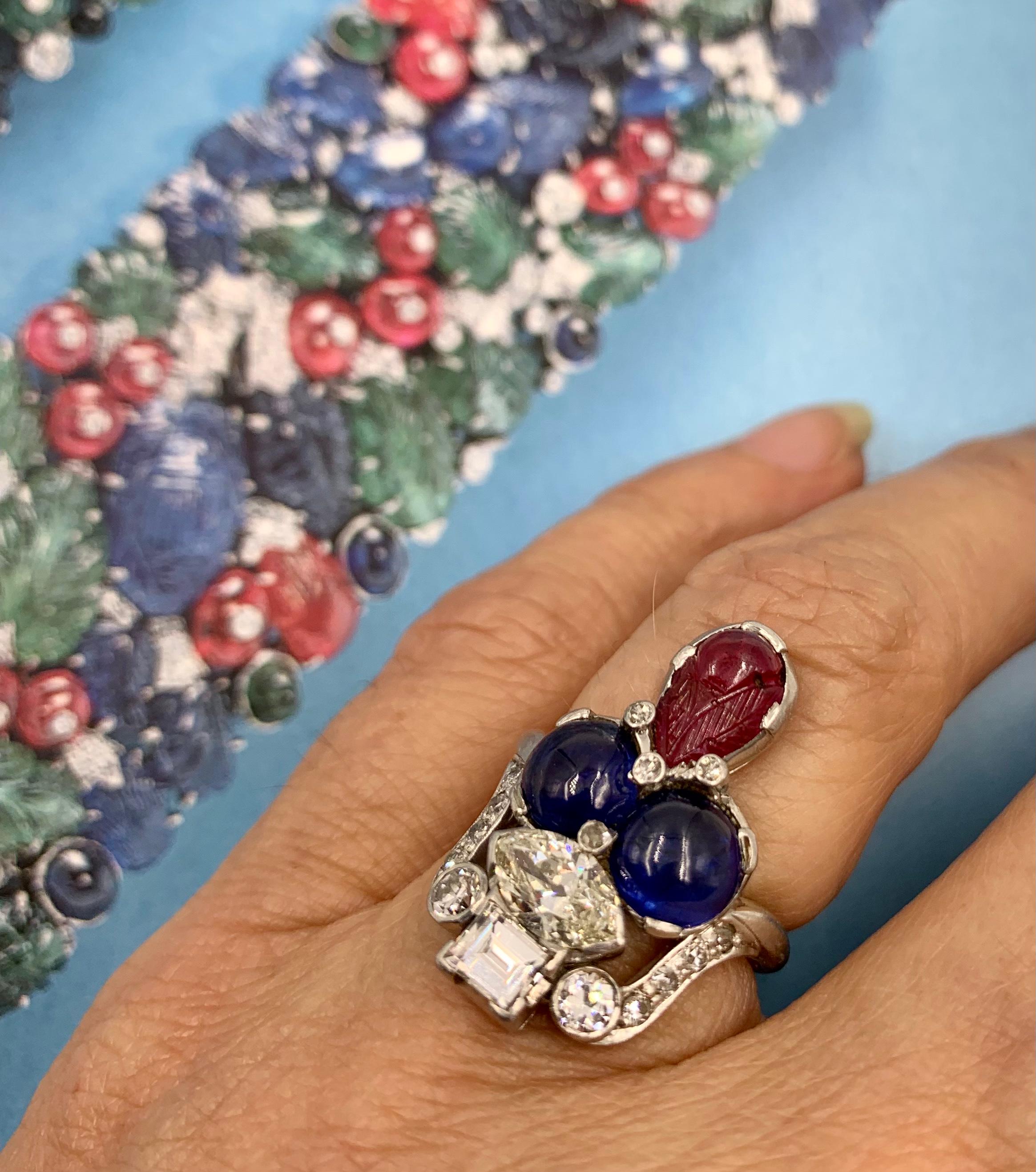 Beautiful, unusual Art Deco period Tutti Frutti diamond, cabochon sapphire, carved ruby ring.
Circa 1920
Designed as a diamond basket laden with cabochon sapphire fruit and carved ruby foliage. The basket centers a 1.2 carat marquise shaped diamond