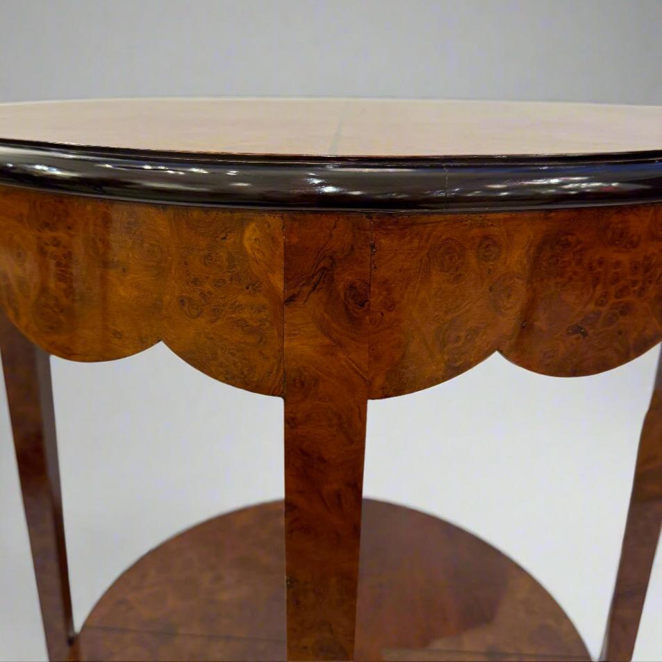 A fine Art Deco period round two-tier side table from France c. 1930. The table is sheathed in a wood veneer and enhanced with ebonized fruitwood inlay. Beneath the circular top is an elegant apron featuring a scallop pattern. Four straight taper