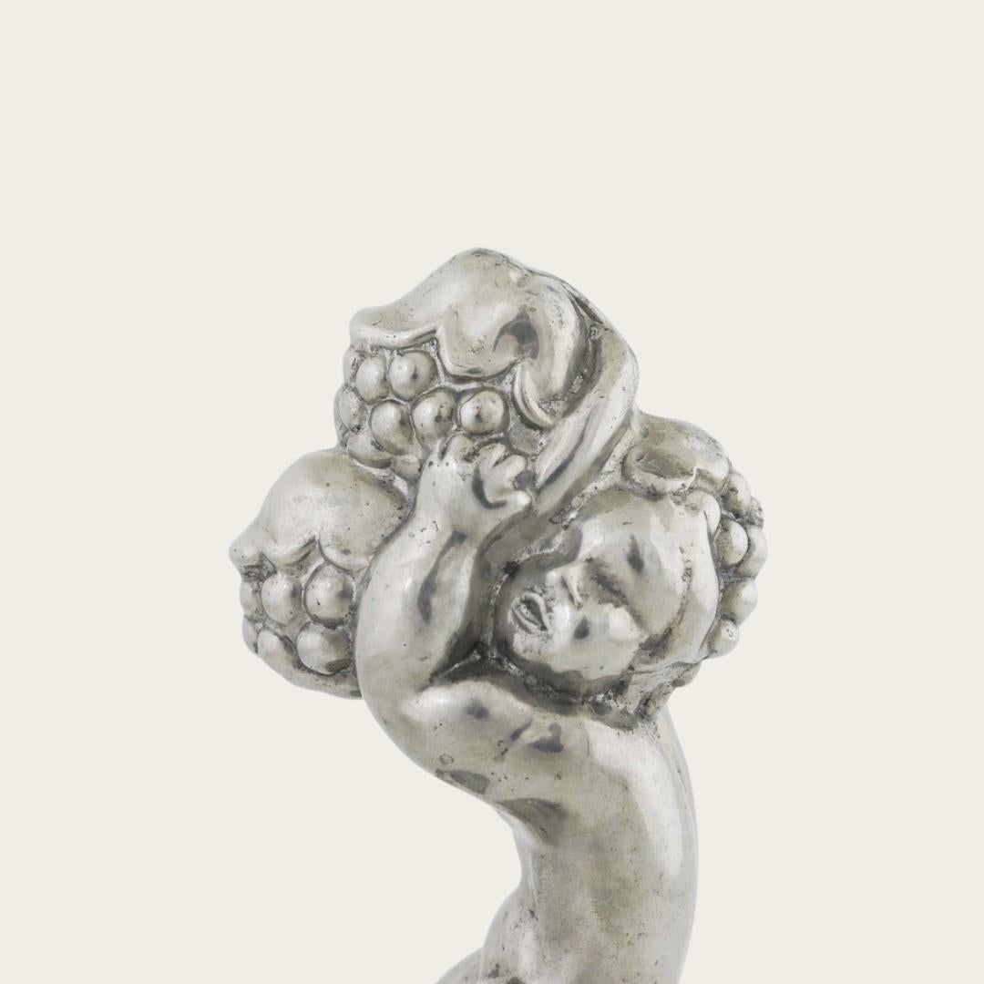 1930s, Denmark. This Art Deco pewter piece, model 841, features a detailed cherub holding blackberries. Designed and stamped by Just Andersen, it carries the maker’s mark on the underside. The piece combines decorative sculpture with practical