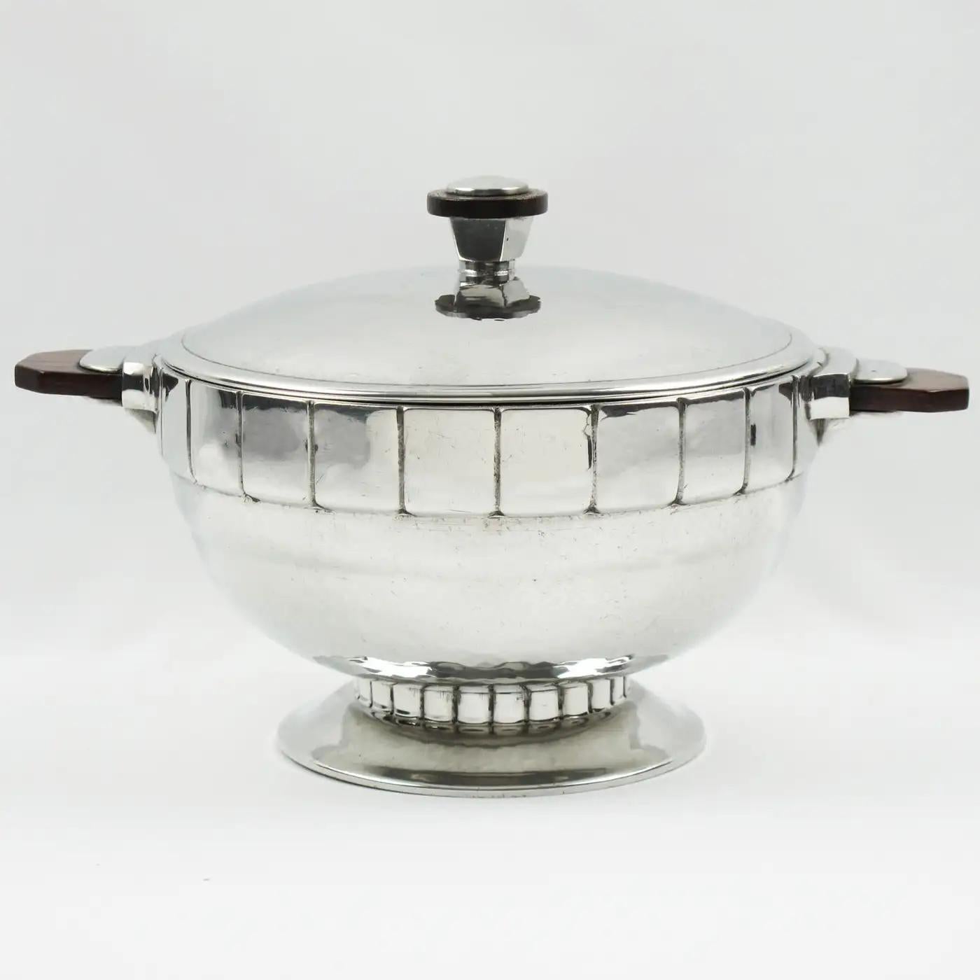 H. J. Swiss Pewter designed this stunning Art Deco embossed polished pewter centerpiece or covered dish in the 1940s. The soup tureen features an elegant modernist shape in polished pewter with a detailed embossed design and solid wood handles. The