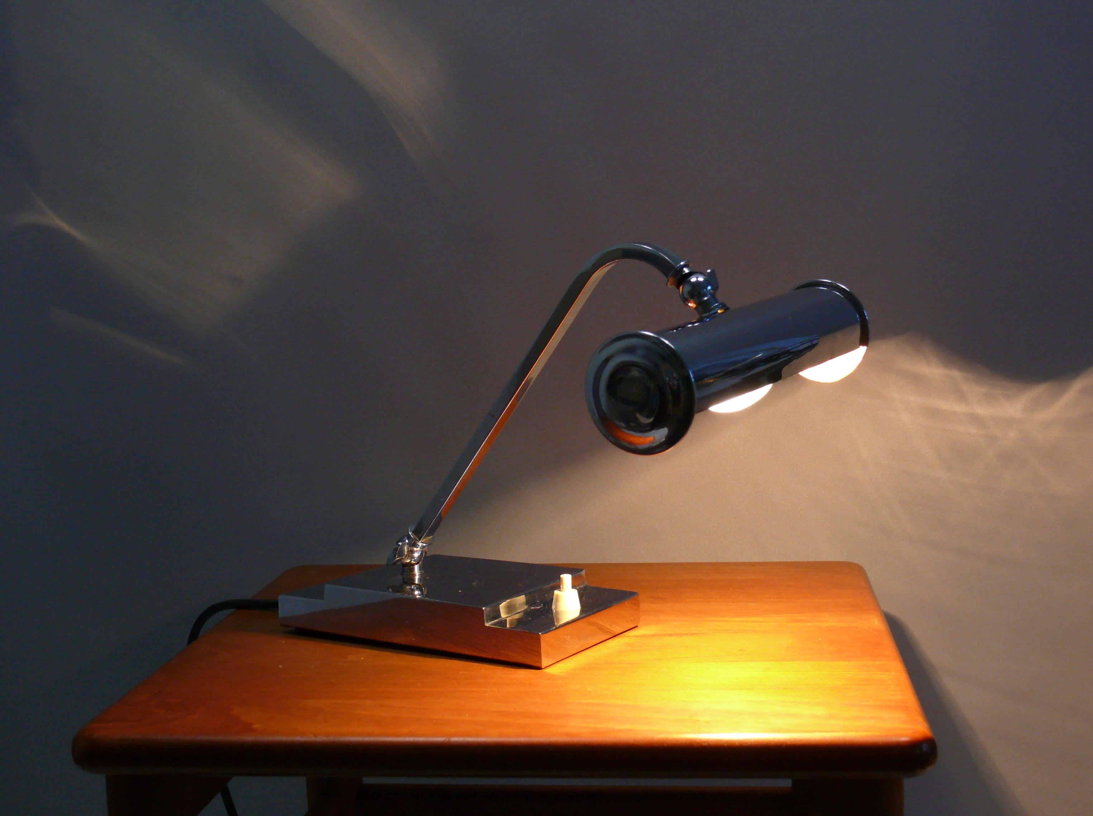 Extraordinary Art Deco piano lamp/table lamp from the 1920s - 1940s, completely chrome-plated with a beautiful, stepped base in the Art Deco style. The lamp is very solidly made and the shade can be tilted using a wing screw, as can the arm. 
The