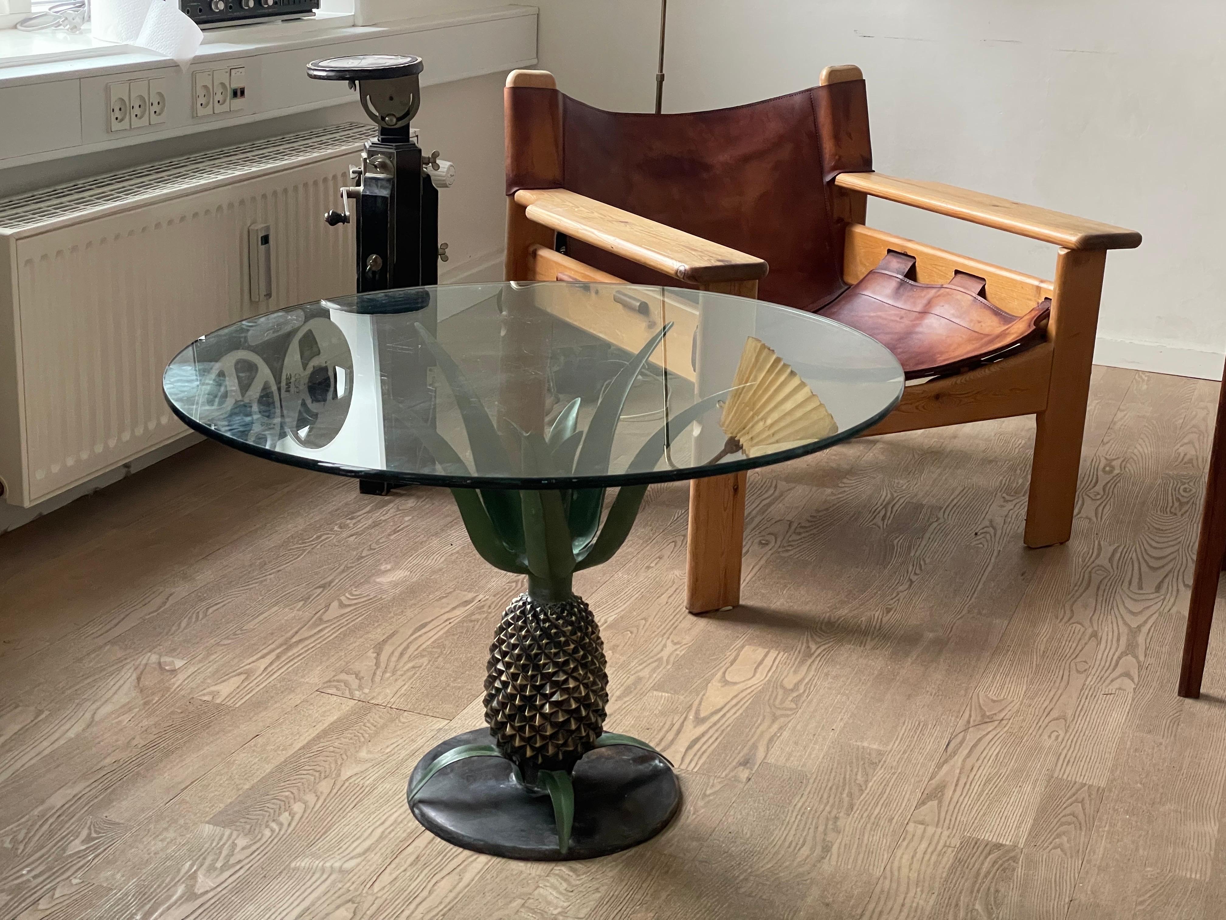 Auténtica declaración de glamour de la Regencia de Hollywood, esta mesa con piña de latón de los años 70 encarna la lujosa fusión de sofisticación Art Decó y elegancia tropical. Elaborada con meticuloso detalle, su escultural base de piña de latón