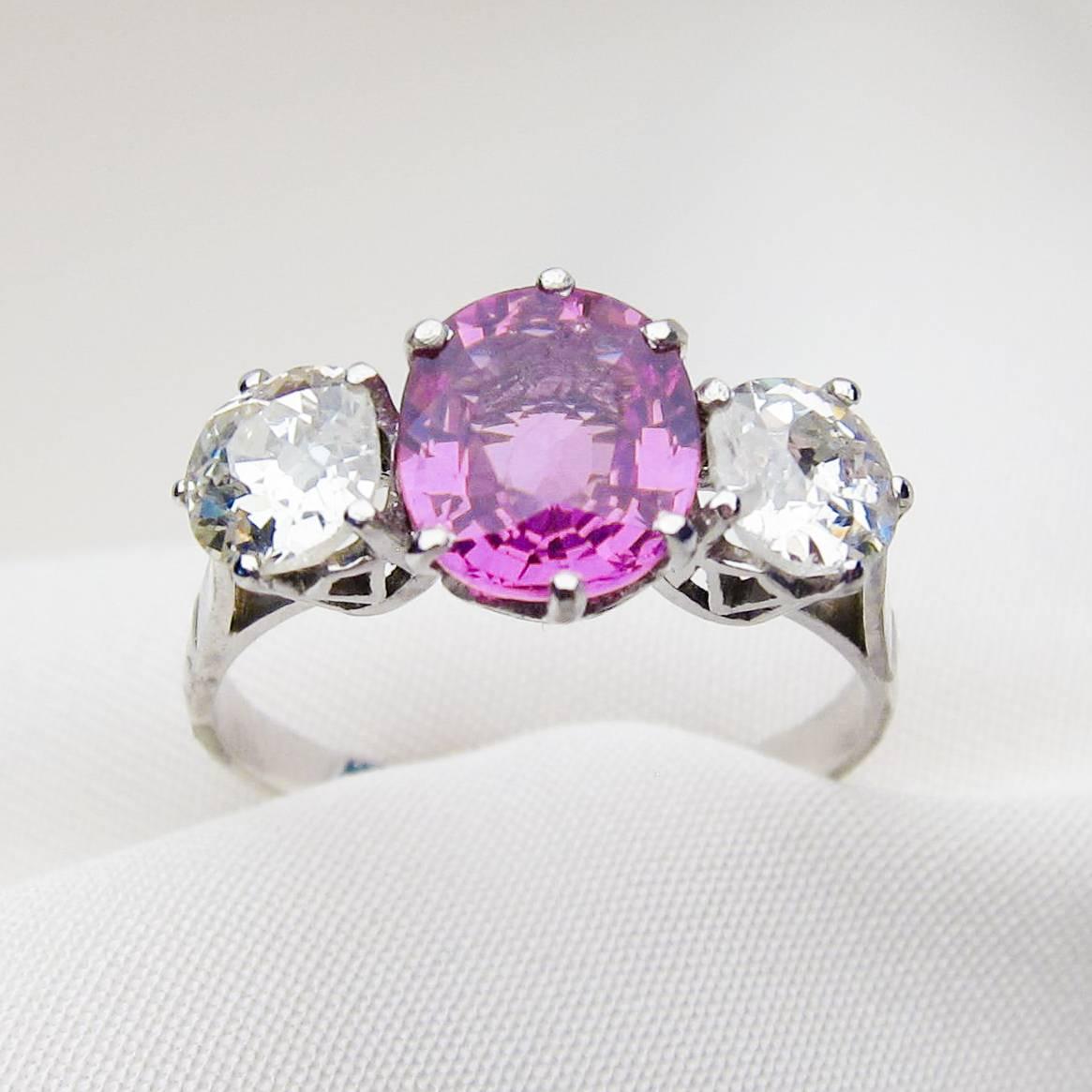 Circa 1920. This lovely platinum Art Deco Era ring features a stunning natural, mixed-cut pink sapphire weighing 1.80 carats. On either side of the sapphire sits a sparkling round old European-cut diamond. The accent diamonds weigh 1.00 carats total