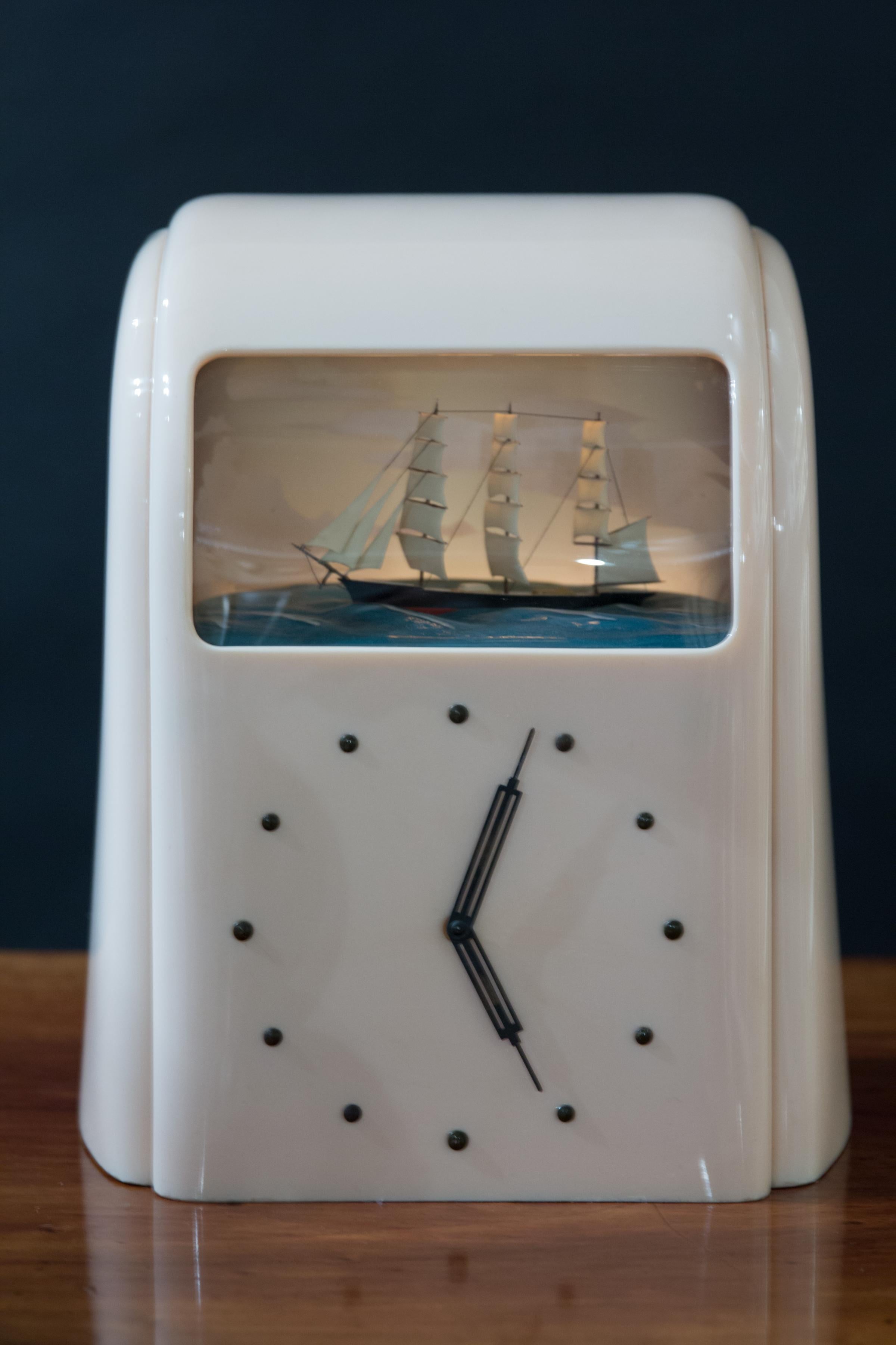Art Deco Vitascope clock with automation rocking ship on an illuminated ocean scene with cloud background. Original ‘Art Deco’ hands with ‘dot’ numerals. 

 Electric movement, ‘pink’ Bakelite case with original green painted back with start wind