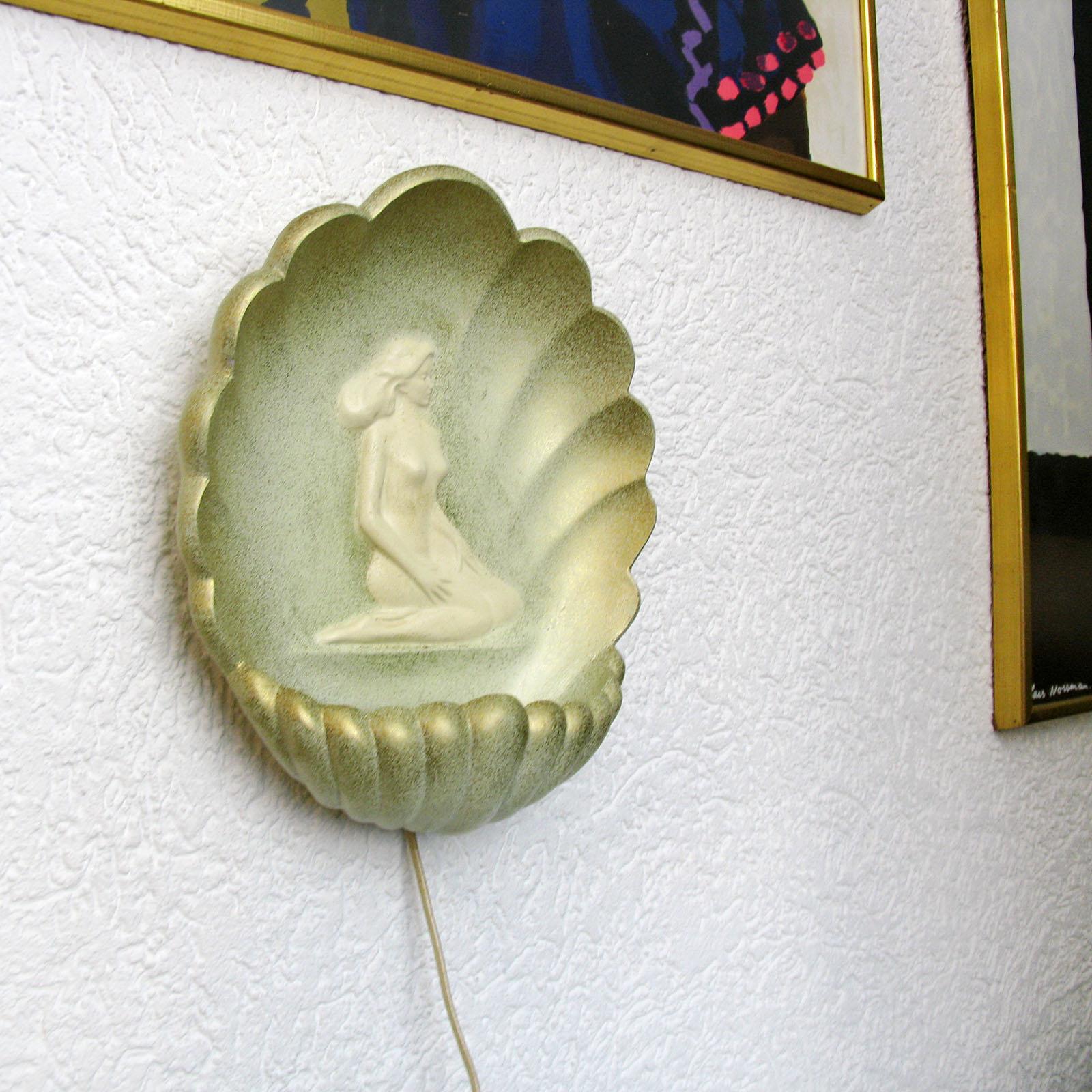 Art Deco plaster sconce wall light, France, 1930s

A beautifully shell shaped wall light. Plaster, with relief nude girl in center, in holds a light in the bottom part. Light green background, white nude, gilt enhancement to the sides.
Very good