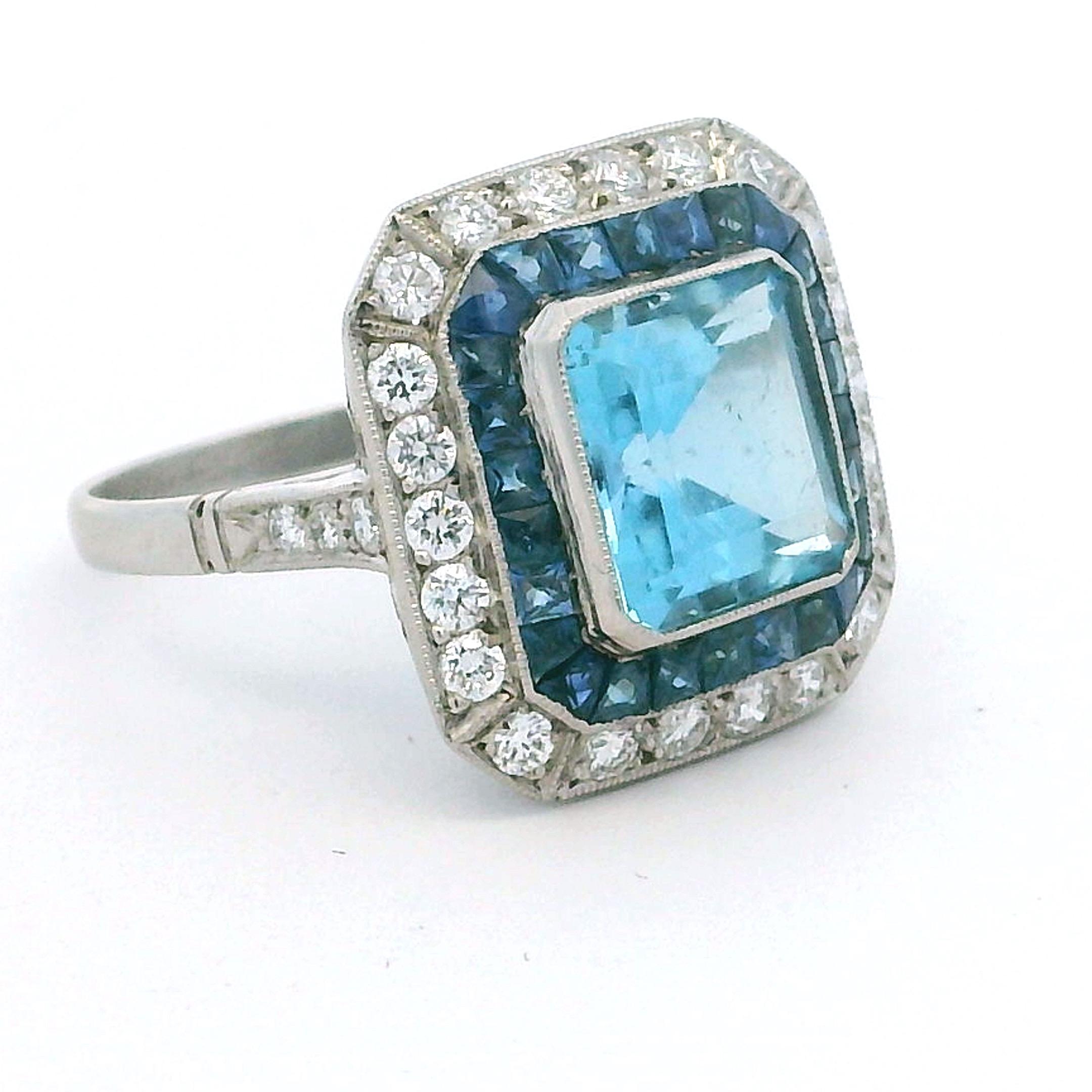 Cette spectaculaire bague Art déco en platine est ornée d'une vibrante aigue-marine de 5,00 carats taillée en émeraude, encadrée d'un double halo spectaculaire de diamants et de saphirs taillés en calibre. L'aigue-marine présente un bleu brillant et