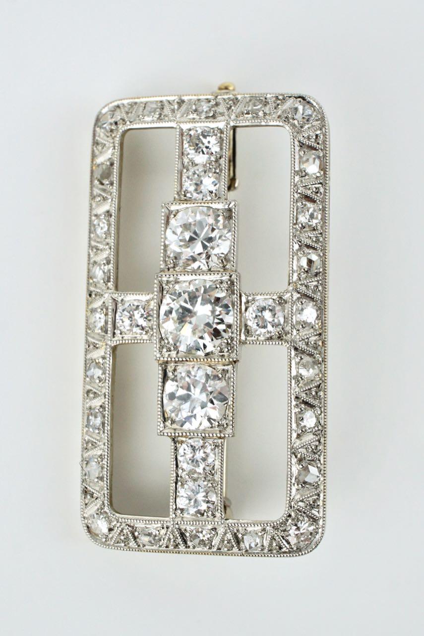 An Art Deco rectangular Platinum and 18k White gold diamond brooch. A beautifully designed and executed pin with a crossbar design of 9 semi modern old European cut diamonds bead set in Platinum on 18ct white gold within a border of alternating