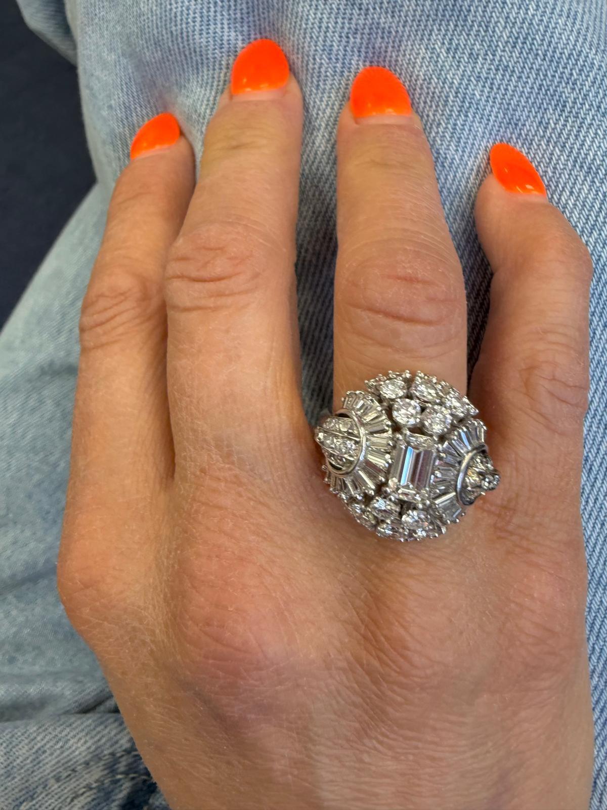 Questo straordinario anello in platino Art Déco è una masterclass di glamour geometrico ed eleganza vintage. Al centro si trova un diamante taglio smeraldo da 0,71 carati, incorniciato da una scintillante serie di 20 diamanti tondi brillanti per un
