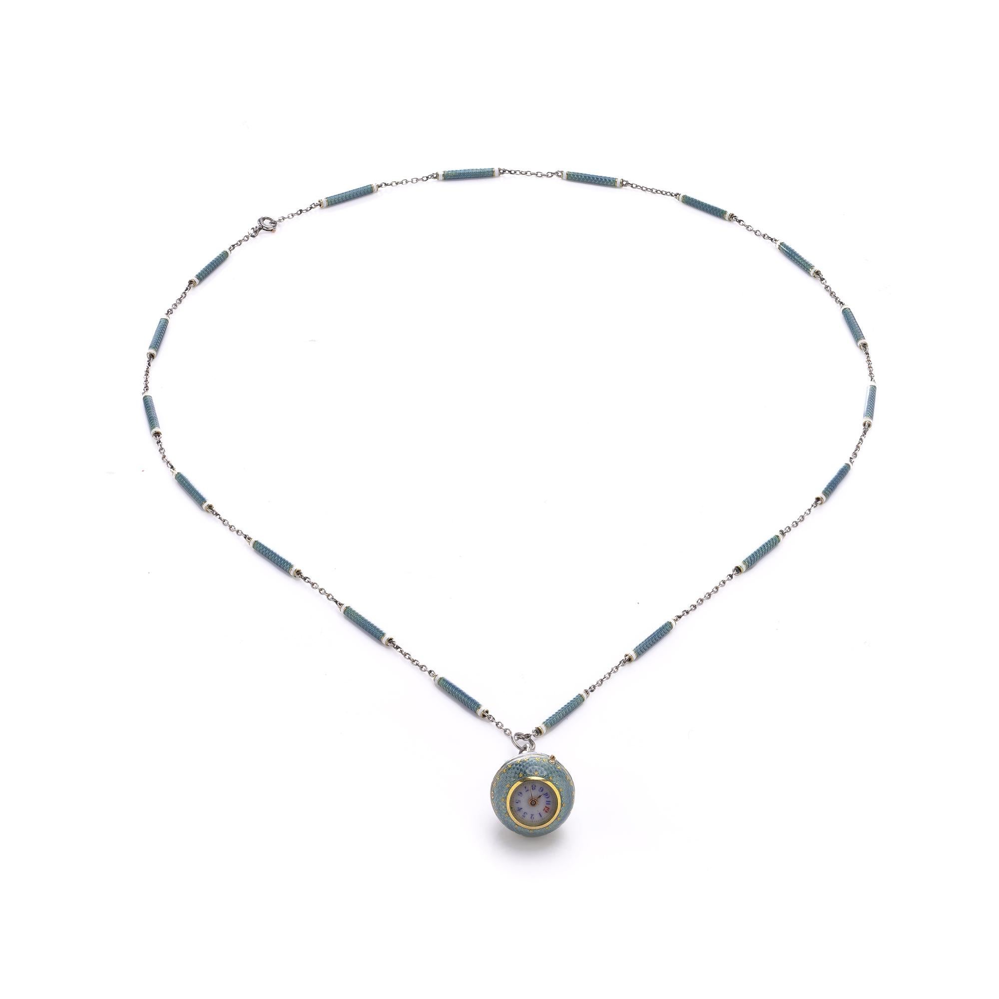 Un'eccezionale collana orologio con ciondolo Art Deco in platino e smalto guilloché realizzata intorno agli anni '20. L'orologio sferico è decorato in smalto azzurro con delicati motivi a stella in oro, sospeso a una catena a maglie in platino e