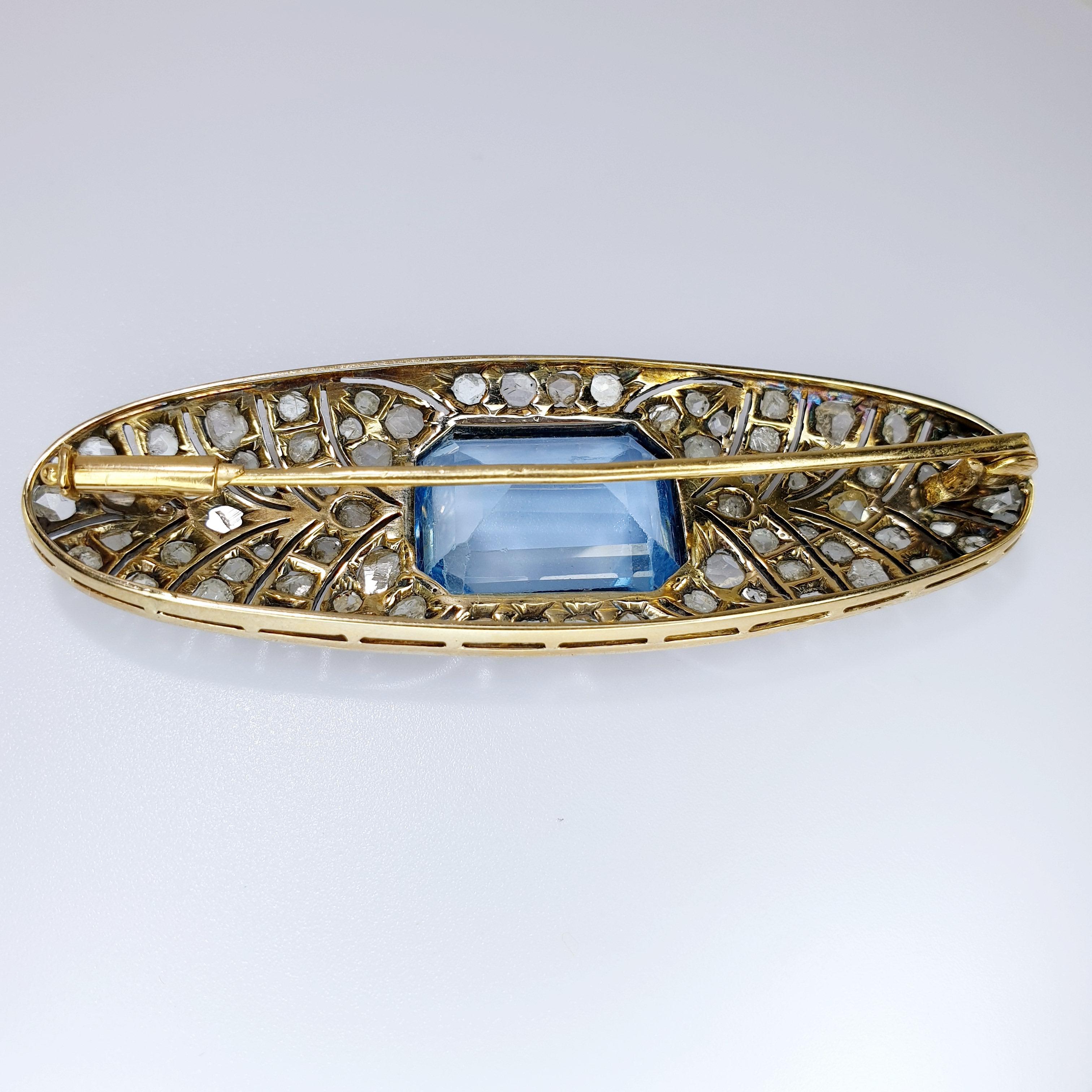 Cette magnifique broche Art déco de forme ovale est ornée d'une pierre centrale de couleur bleue taillée en émeraude.
Les diamants de taille ancienne reposent sur une bande de pointes sur une base en platine et un revers en or rose 18 carats. 

PRÊT