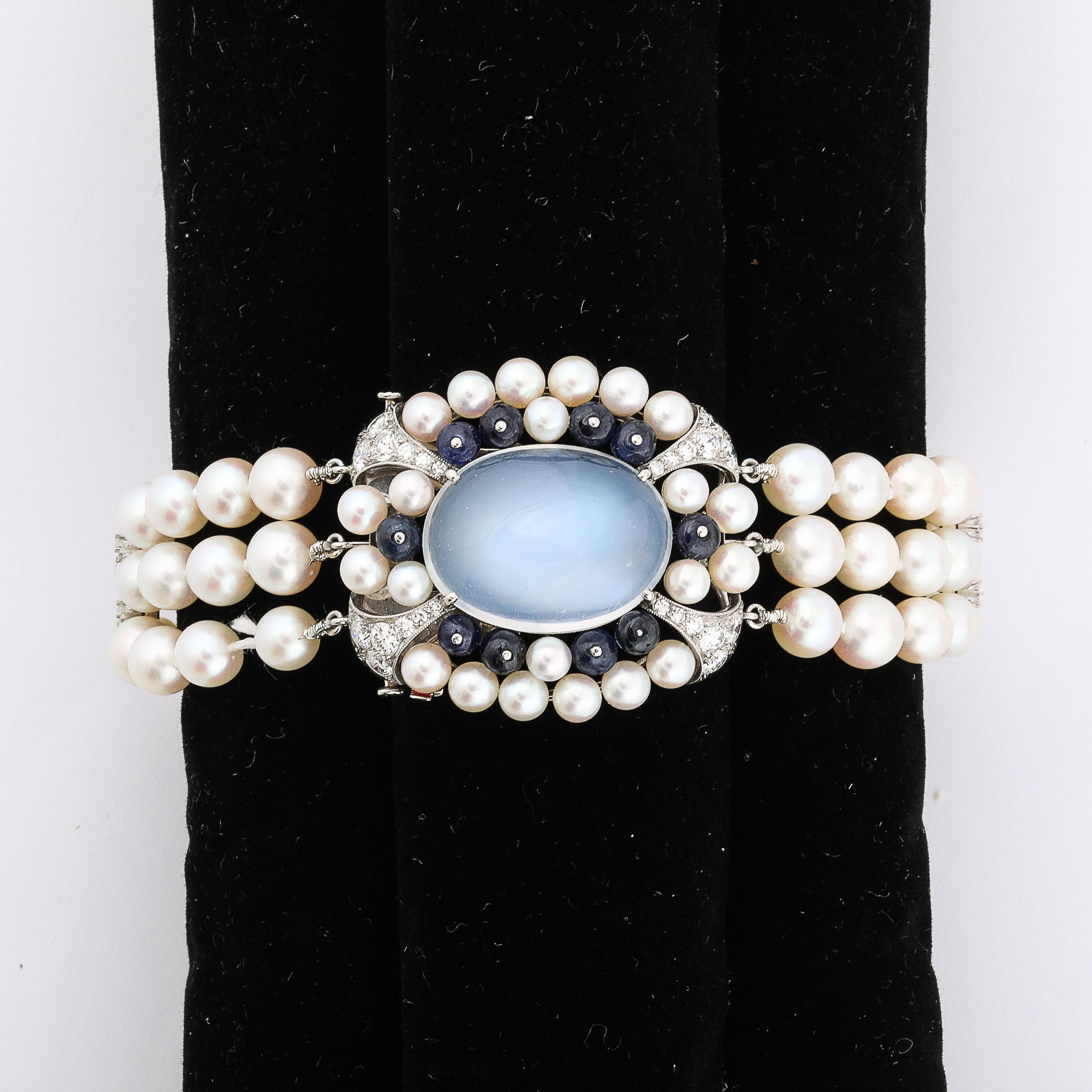 This uniquely elegant Art Deco Platinum Bracelet 21.58 Ctw Gems and Moonstone by Raymond C. Yard is designed and fabricated in the United States, Circa 1940. The main element is highly adorned with natural gemstones and features an oval cabochon cut