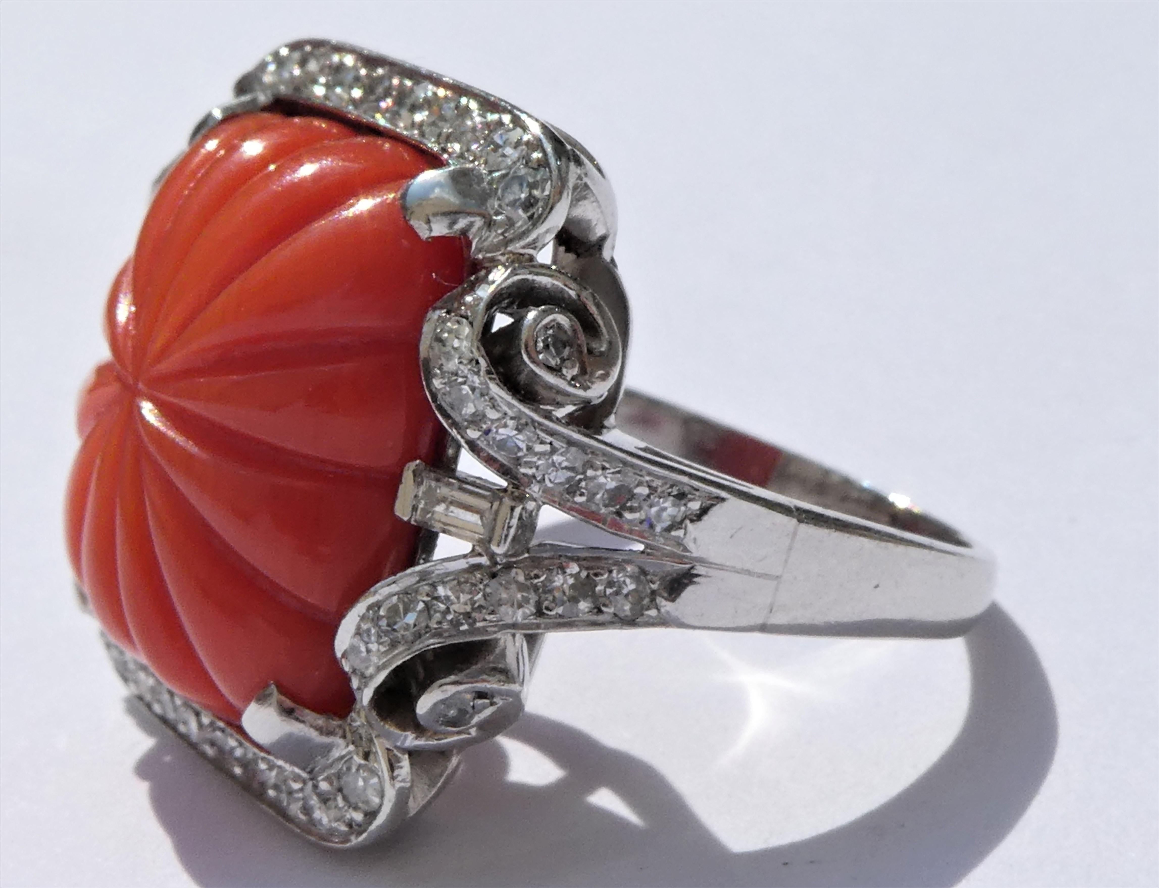 This ring was crafted circa 1930 in platinum with a carved domed Sardegna coral cabochon from the island of Sardinia in the center. Accentuating the red coral there are 52 round single cut diamonds and 2 diamonds in baguette cut with a total of
