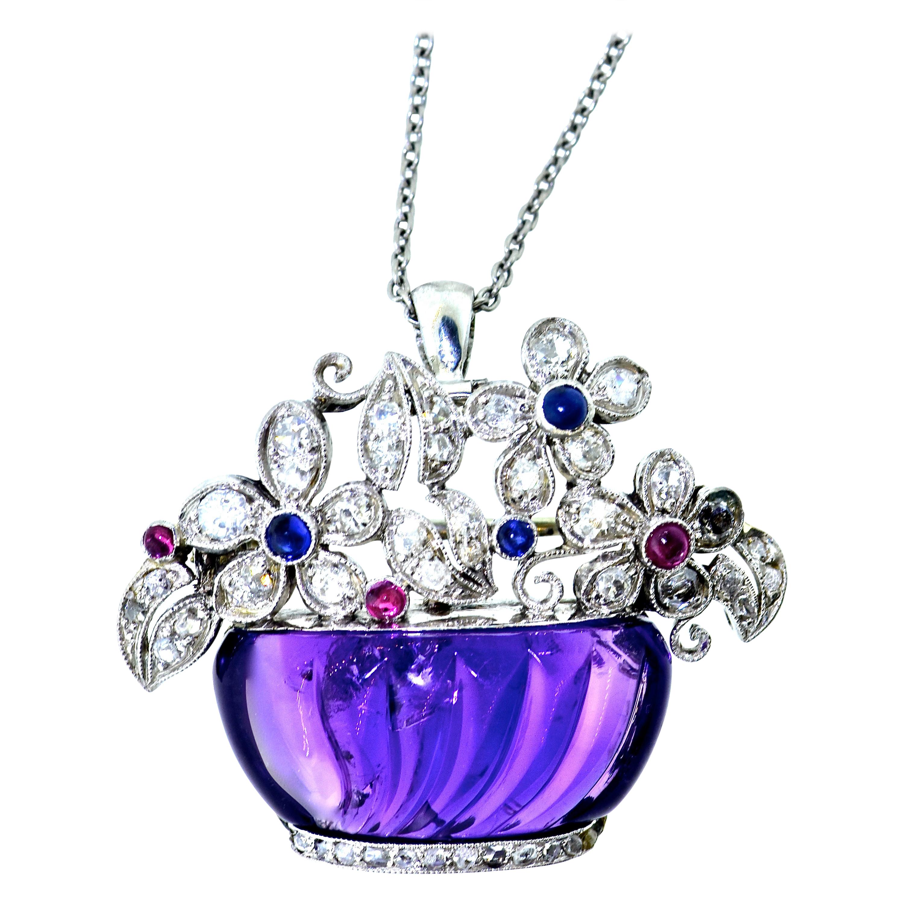Art Deco pendant with a carved natural amethyst (probably Siberian because of the presences of reddish undertones), creates a platinum, diamond, sapphire and ruby basket of flowers.  Capable of being worn as a pendant or brooch, this charming piece,