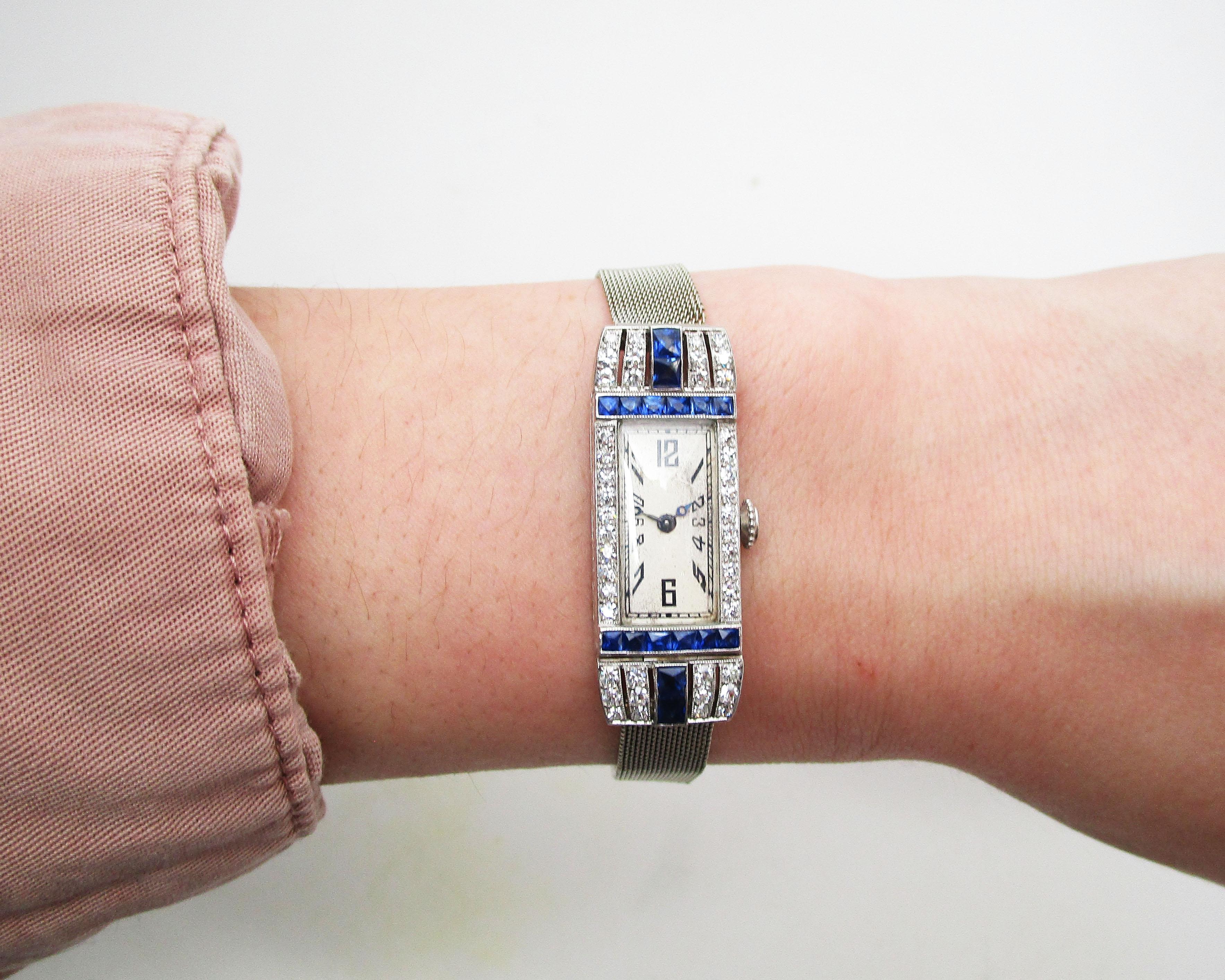 This is a breathtaking Art Deco watch with a platinum case set with sparkling white diamonds and royal blue calibre sapphires paired with a flexible mesh 18k white gold strap. This watch truly defines Deco with its long layout and strong geometric