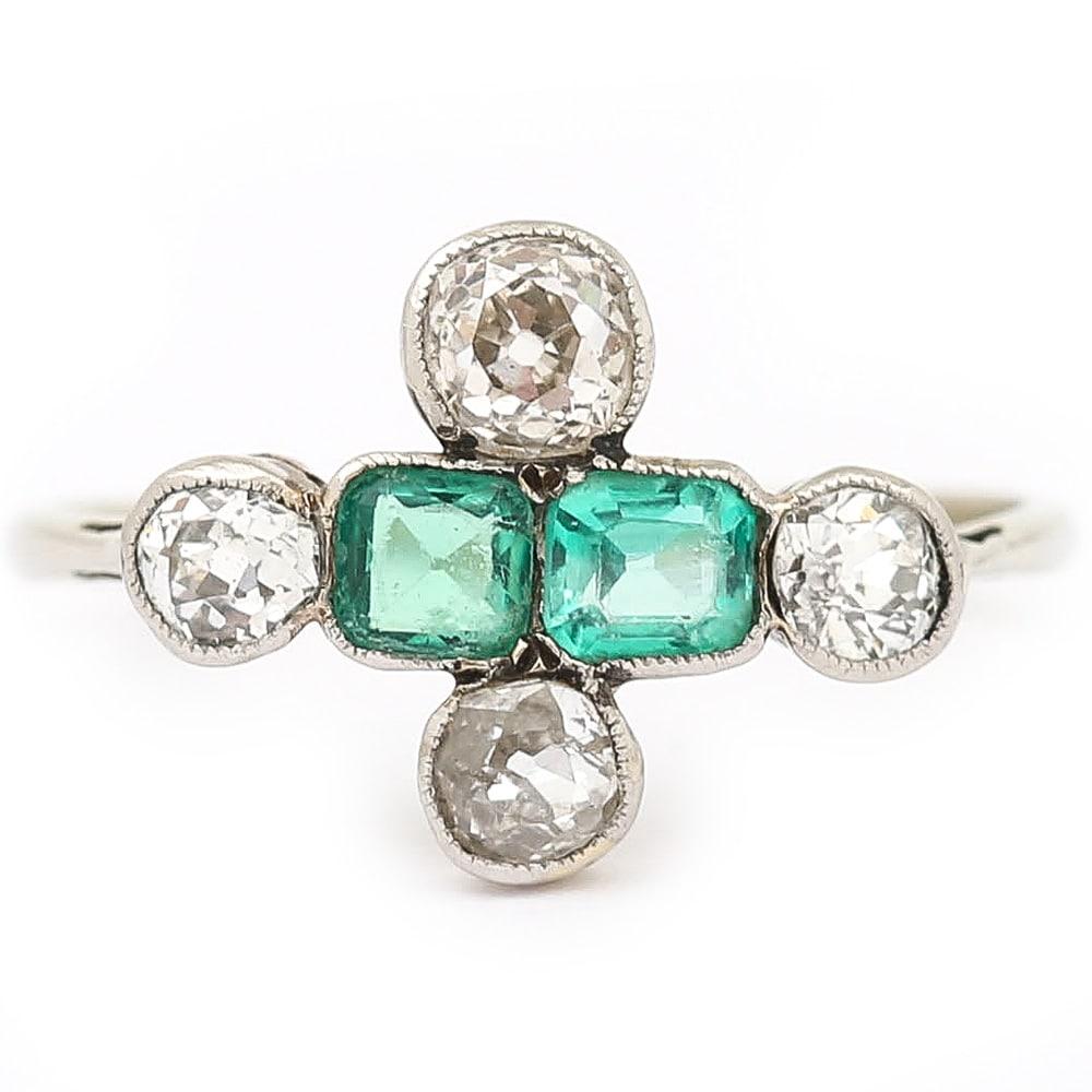 A delightful platinum Art Deco period ring with four Old Mine cut diamonds of varying size with two unmatched emeralds, formed into a cruciform design. This pretty antique ring is in a simple form consisting of four Old Mine cut diamonds with a