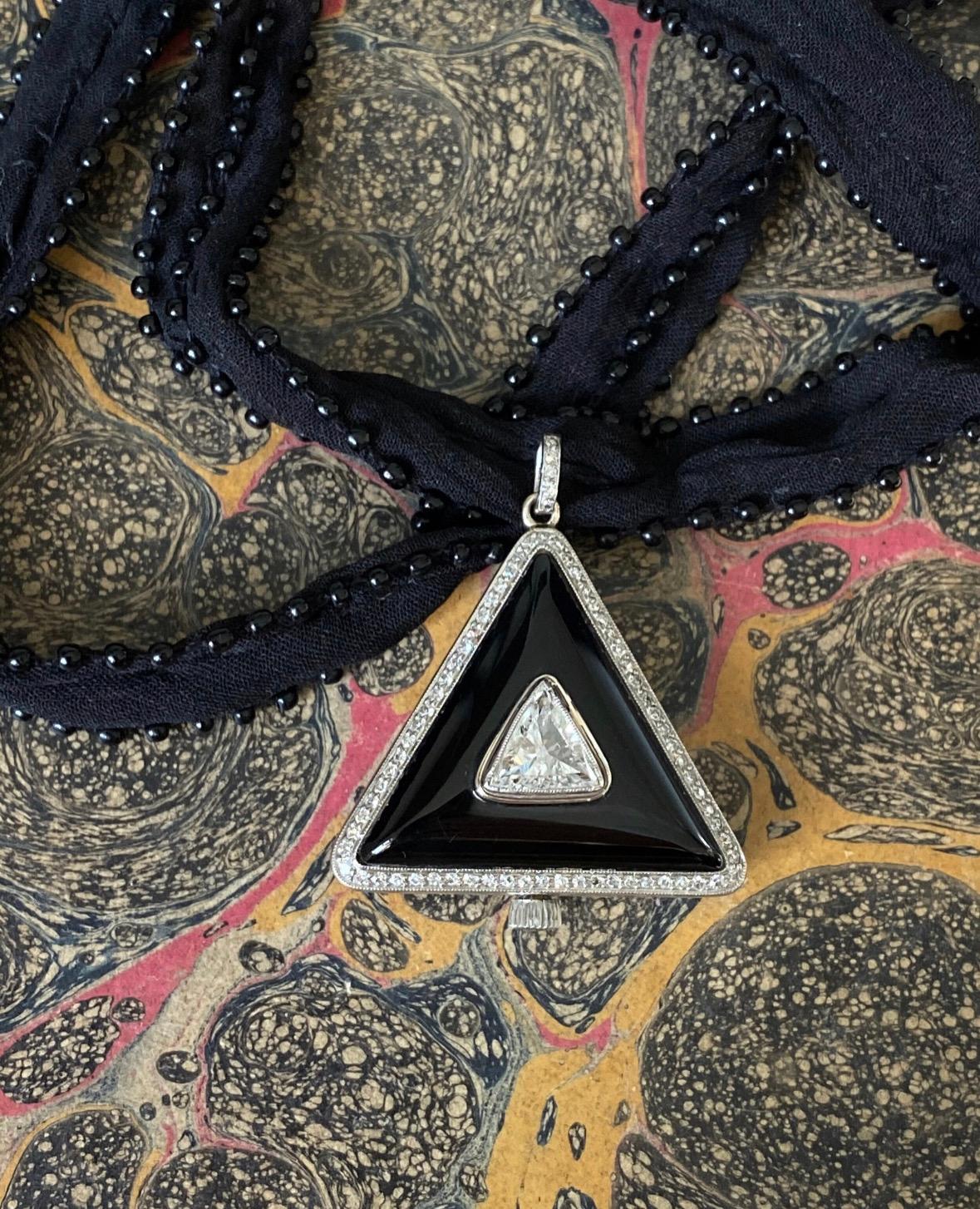 This sleek and striking Art Deco pendant watch centers on a sparkling triangular-cut diamond mounted within a domed glossy black onyx plaque framed in a border of single-cut diamonds. The watch boasts a silvered dial with black Roman numerals and