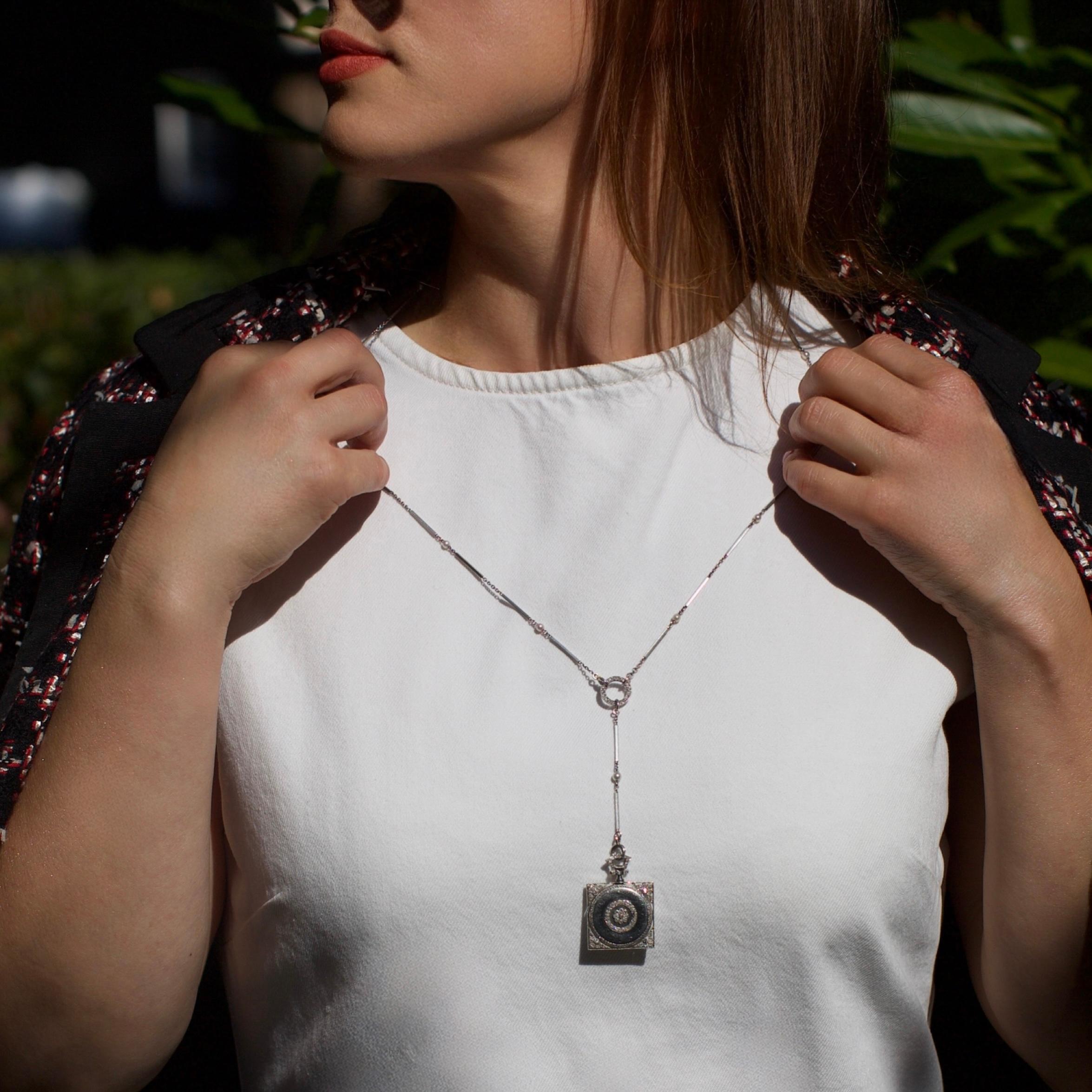 Collier-montre en platine de style Art Déco, composé d'une chaîne géométrique sertie de perles naturelles et de diamants, suspendu à un boîtier de montre carré. L'étui est décoré de motifs feuillagés gravés et de détails en millegrain, son revers