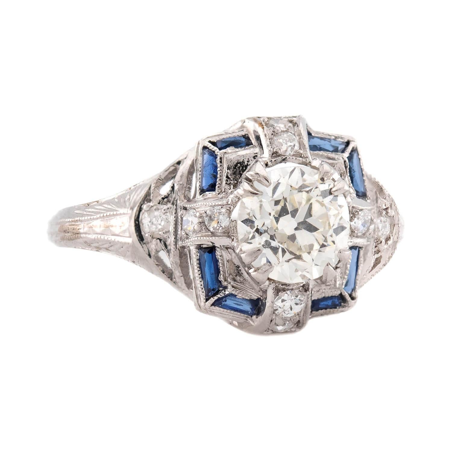 An absolutely beautiful diamond and sapphire engagement ring from the Art Deco (ca1930s) era! Crafted in platinum, this ring features a central 1.62ct old European cut diamond held within a multi-prong setting. The diamond rests atop a square-shaped