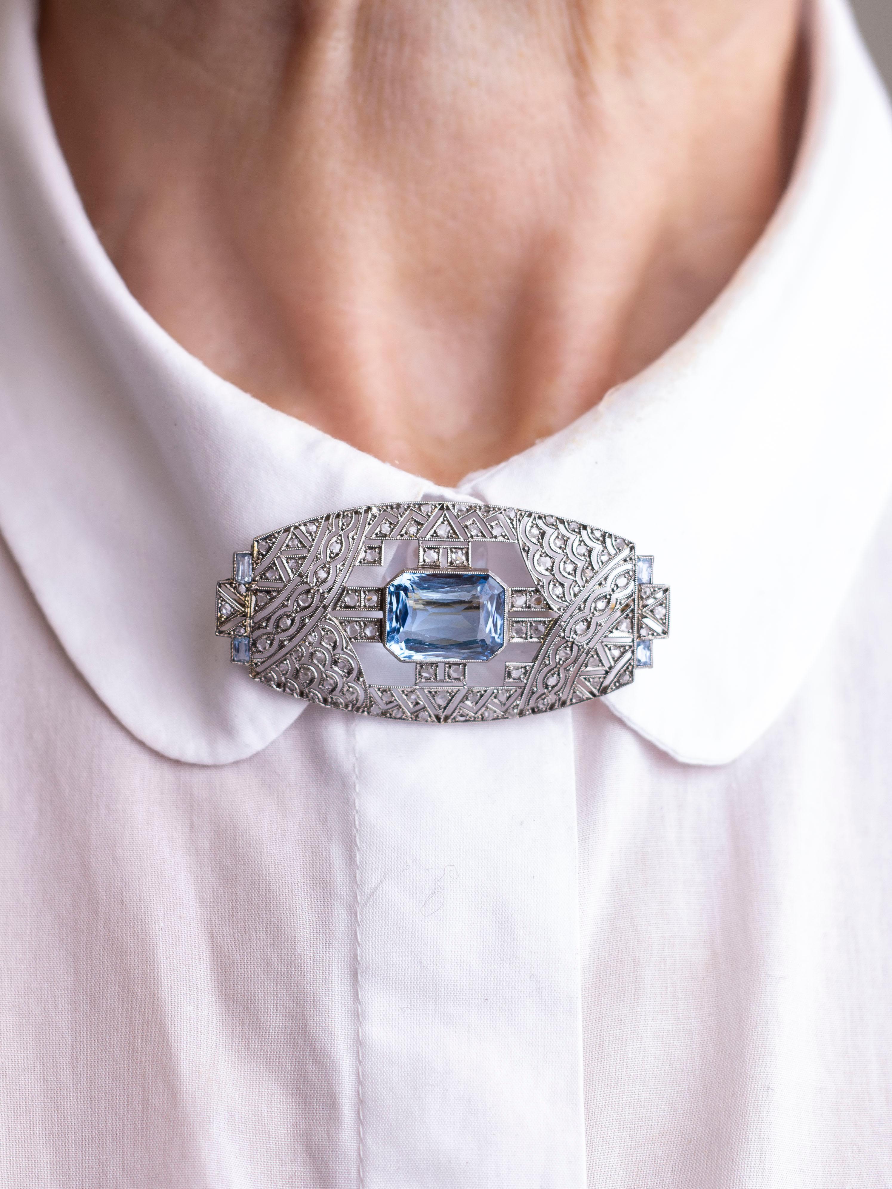 This stunning Art Deco brooch pin has been crafted from platinum and set with bright aquamarines and old cut diamonds. The central aquamarine is an emerald cut stone weighing 8.10 carats that has been rubover set. To the corners of the brooch are a