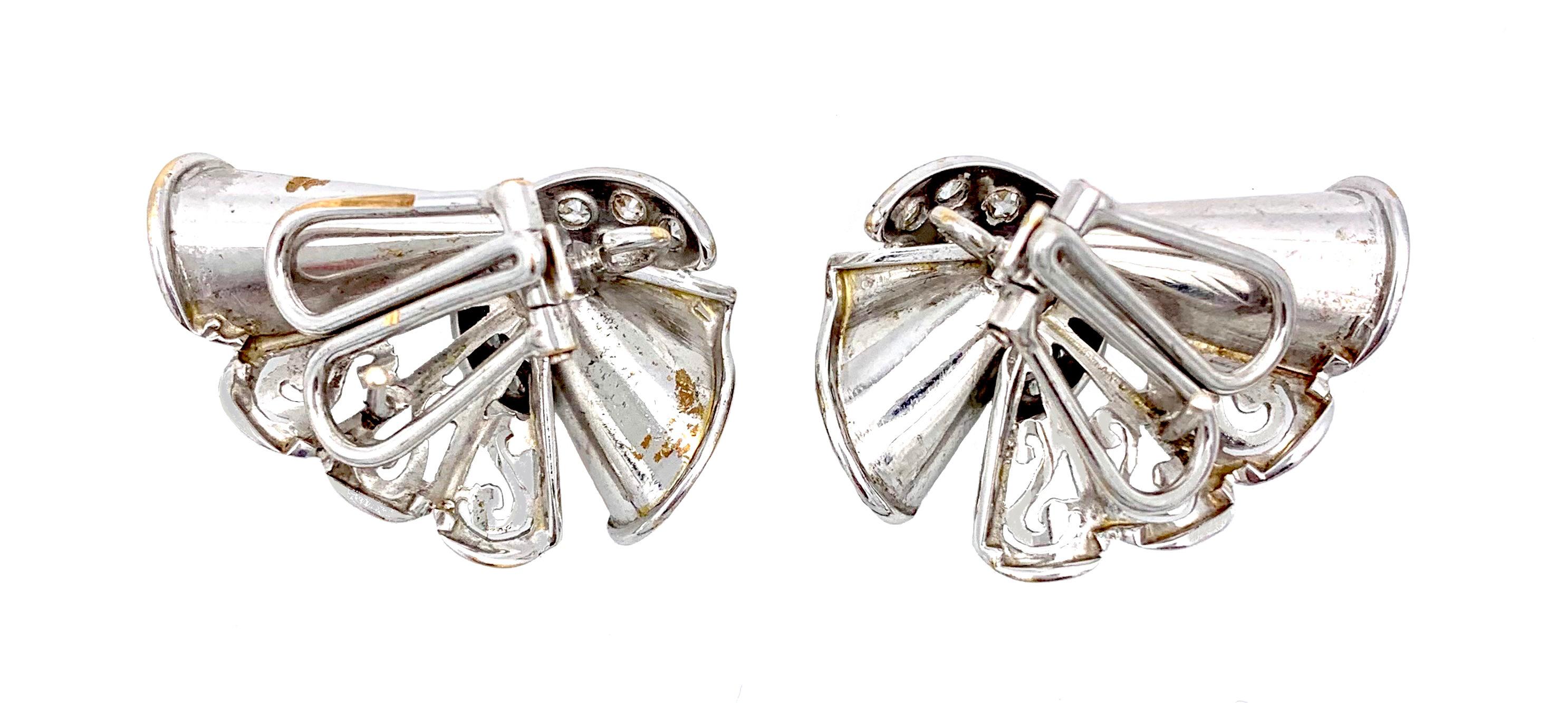 These Art Deco Clip-on Earrings were made out of 14 Karat gold and have then been rhodium plated. The design shows scrolls with pierced  elements reminiscent of lace. The gold fabric is held together by a crescent shaped element set with brilliant