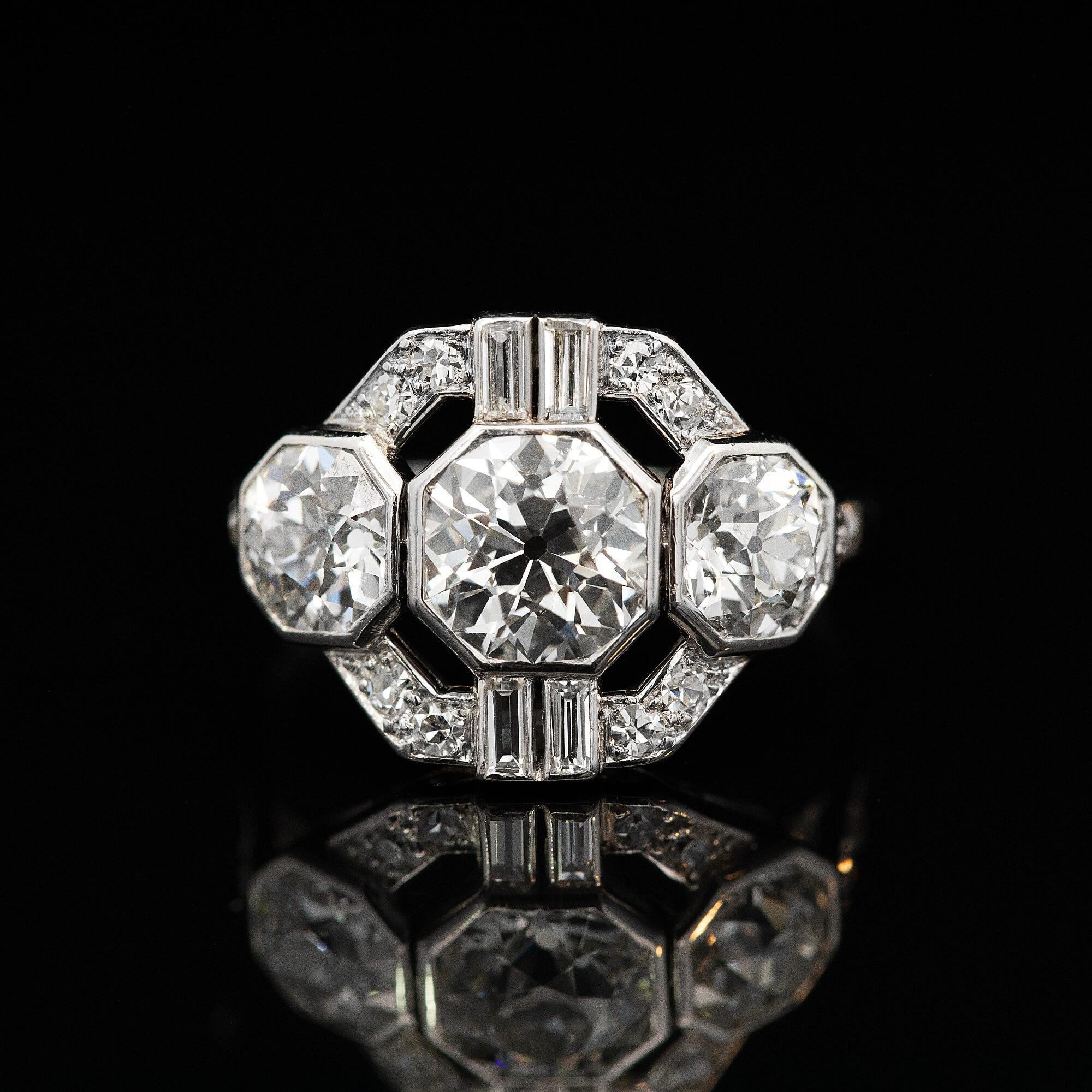 Ein geometrischer Art-Deco-Cluster, bei dem die größeren Diamanten in sechseckigen Lünetten gefasst sind. Dieser Ring erstreckt sich über den ganzen Finger und ist bis zum Fluchtpunkt mit Diamanten besetzt. Trueing, dieser Ring bringt das glamouröse