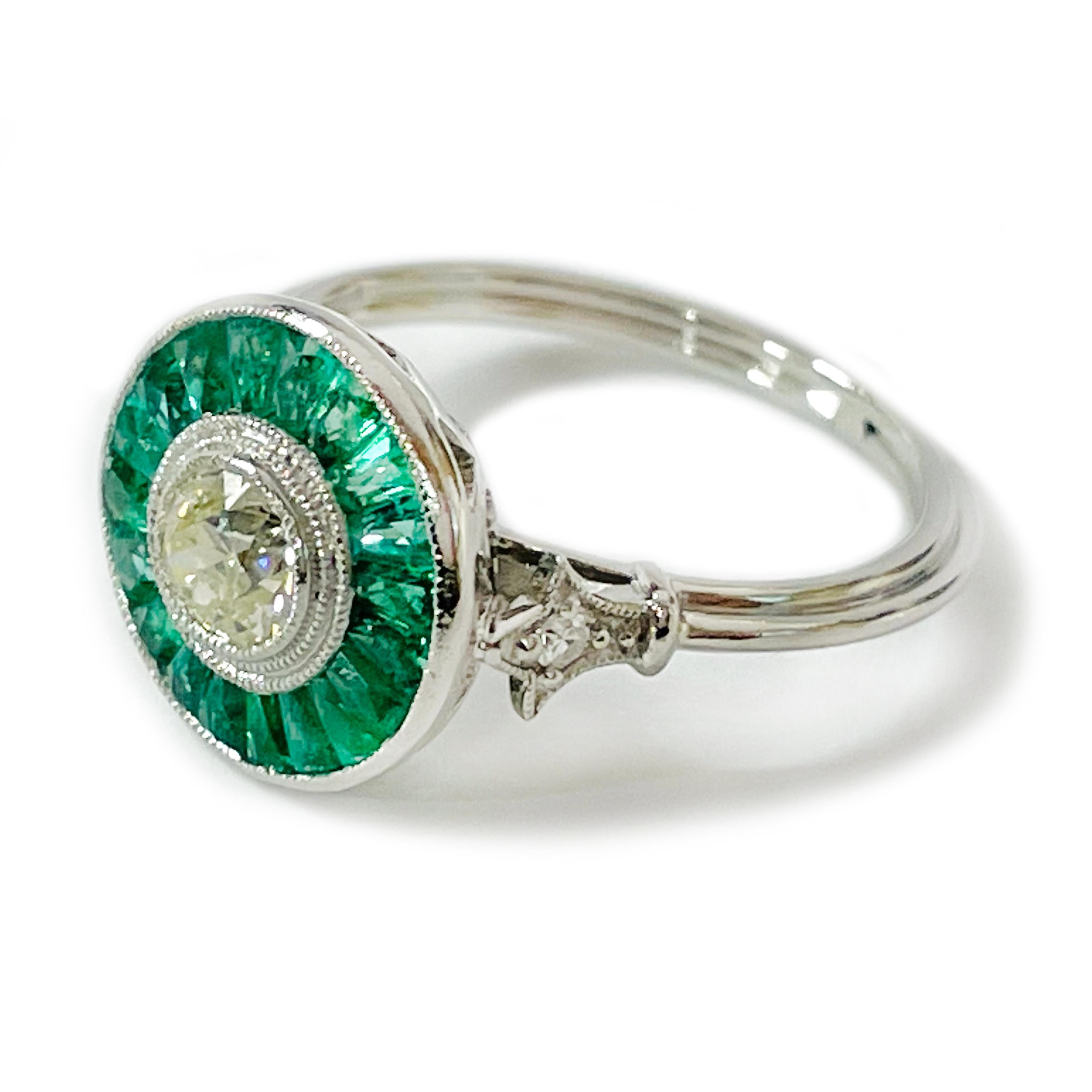 Art Deco Platinum Emerald Diamond Ring. The stunning ring features a center bezel-set round diamond and two round side diamonds, the total carat weight of the three diamonds is 0.90ctw. There are 2.5 x 1.5mm emerald tapered baguettes channel-set in