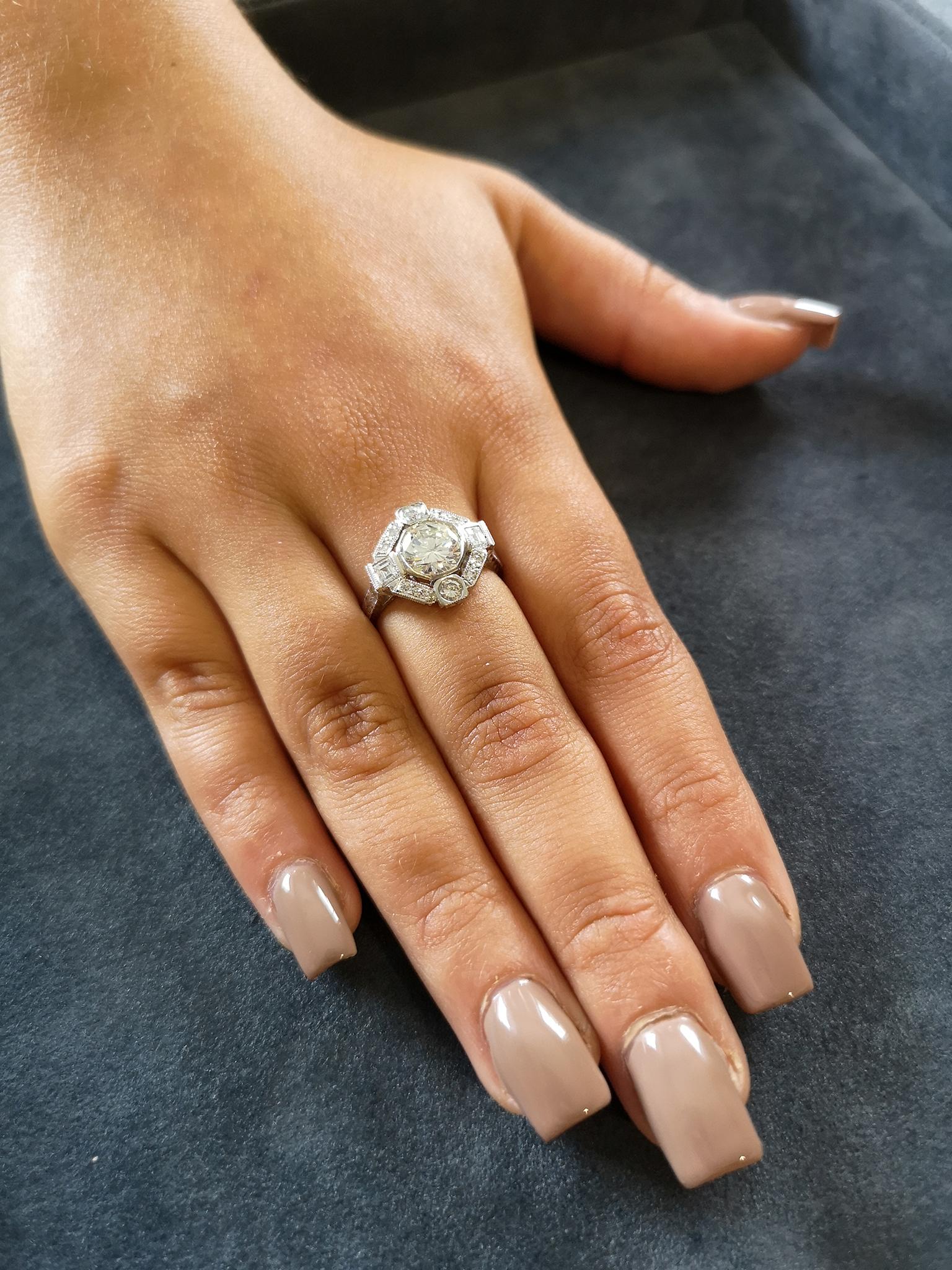 A beautiful and elaborate Art Deco diamond ring in platinum. A central brilliant-cut diamond of approximately 1.40 carats, I colour, VS clarity. Mounted in a bezel setting, surrounded by three pavé diamond set 'bars' interspersed with four